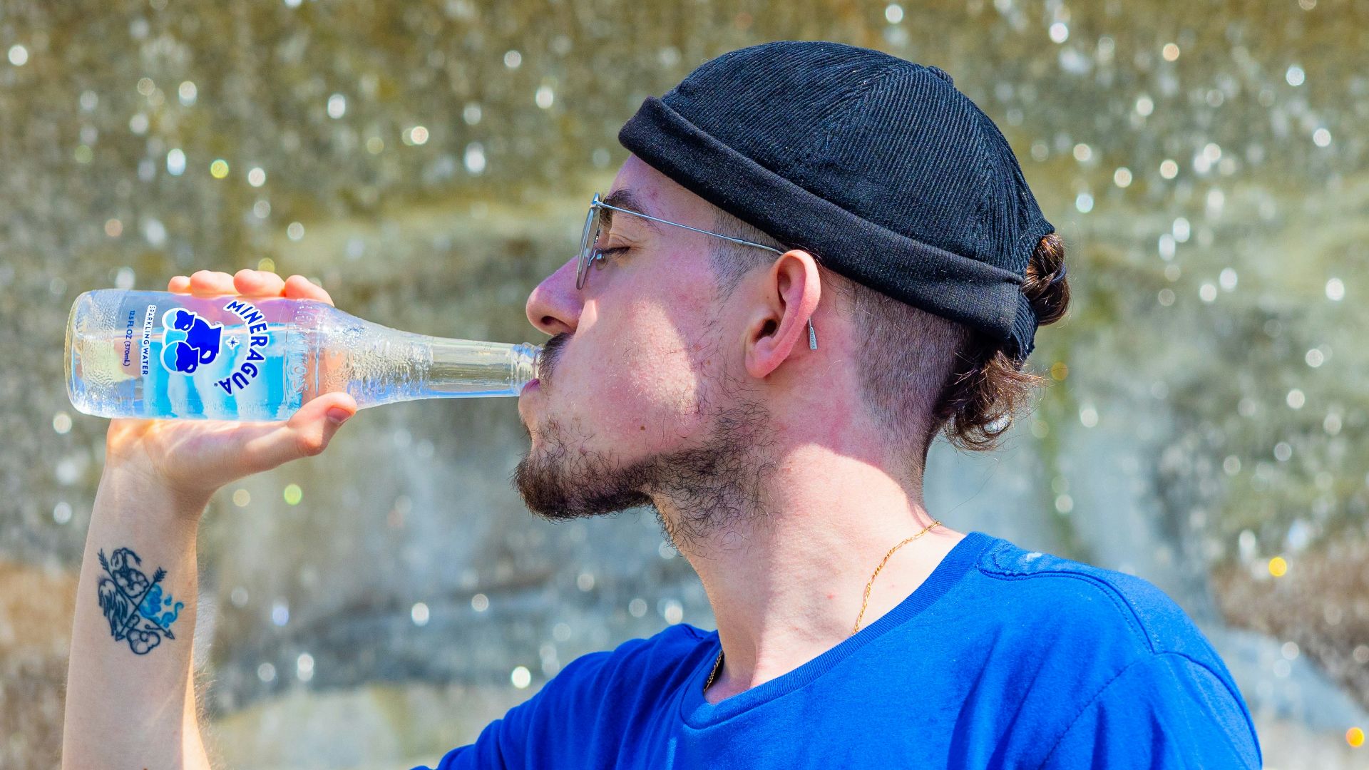 a man drinking water from a bottle in front of a fountain