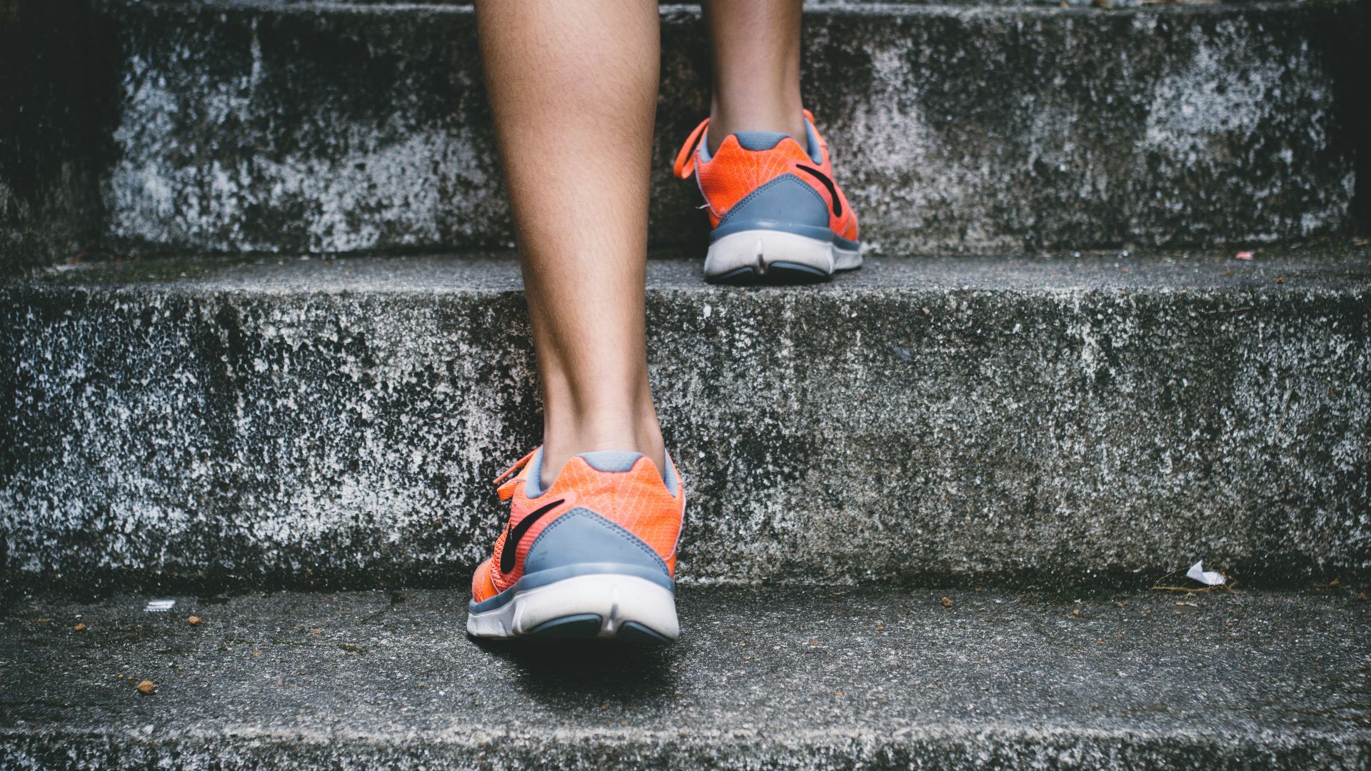 person wearing orange and gray Nike shoes walking on gray concrete stairs