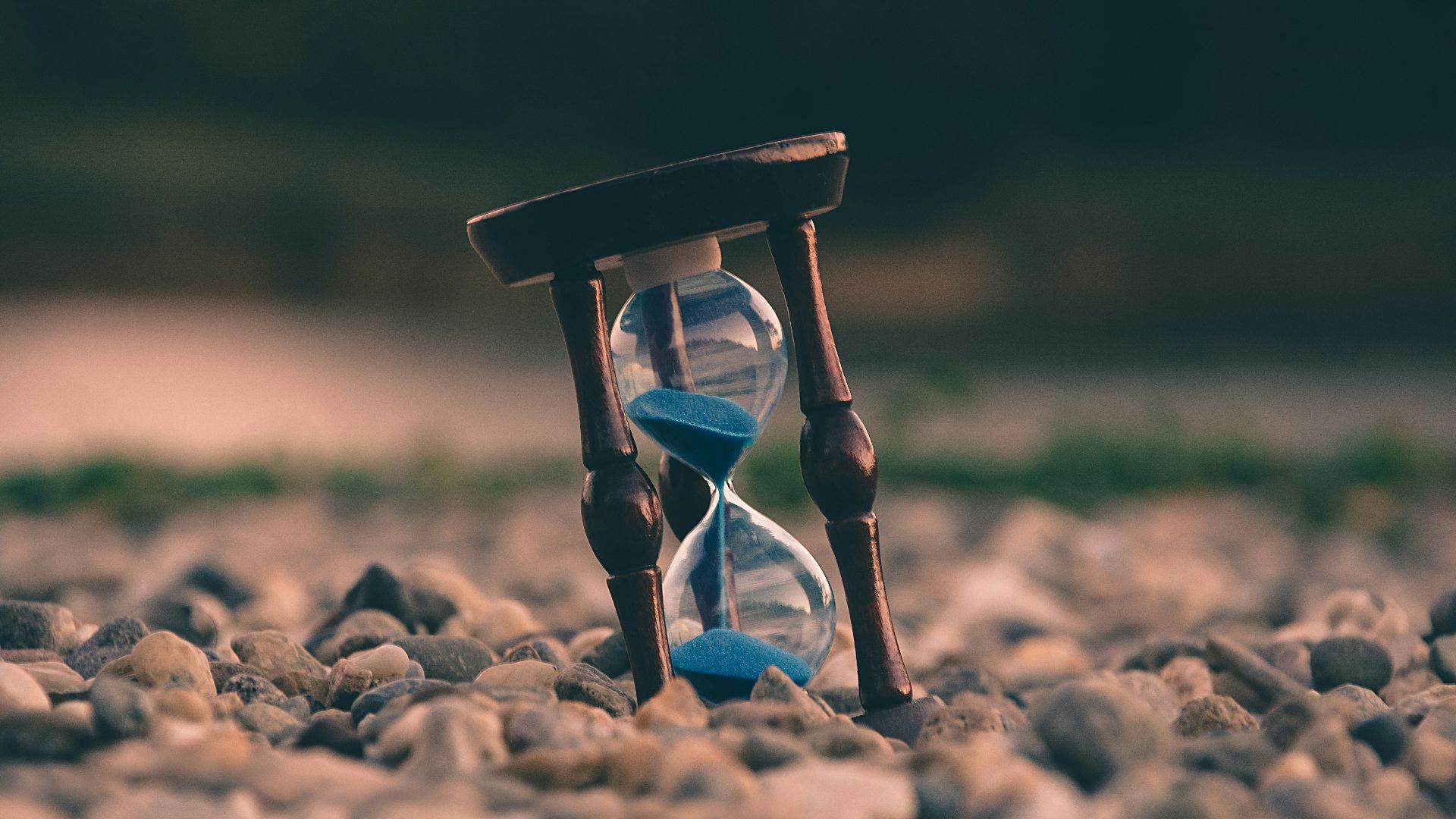 selective focus photo of brown and blue hourglass on stones