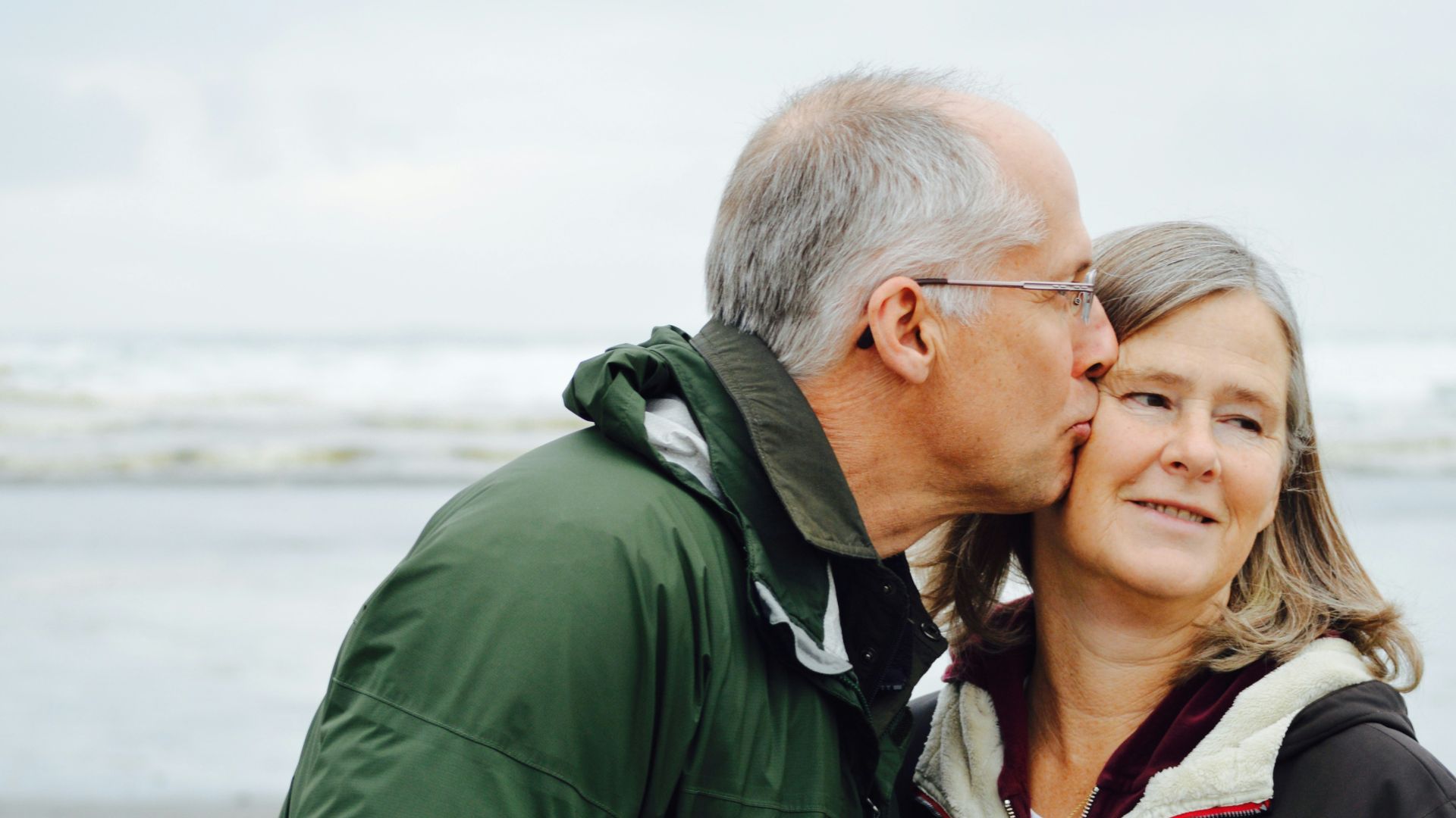man kissing woman on check beside body of water