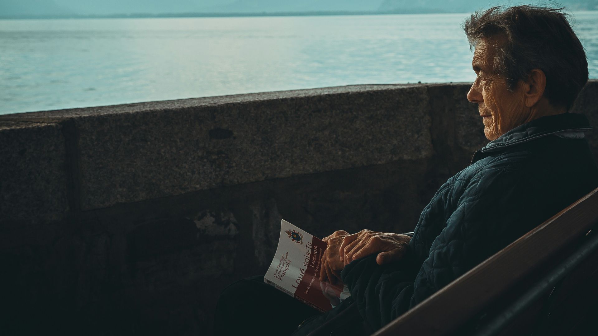 man sitting while holding a book watching on body of water