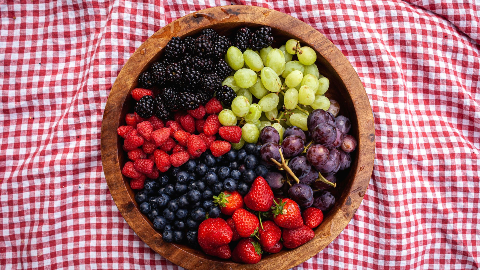 a wooden bowl filled with berries and grapes