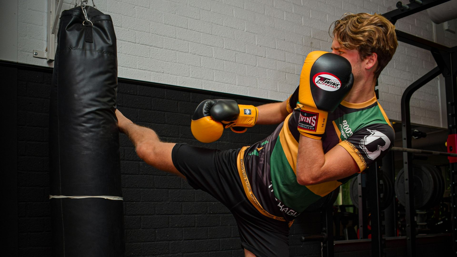 woman in green and black stripe tank top and black shorts carrying black and red boxing bag