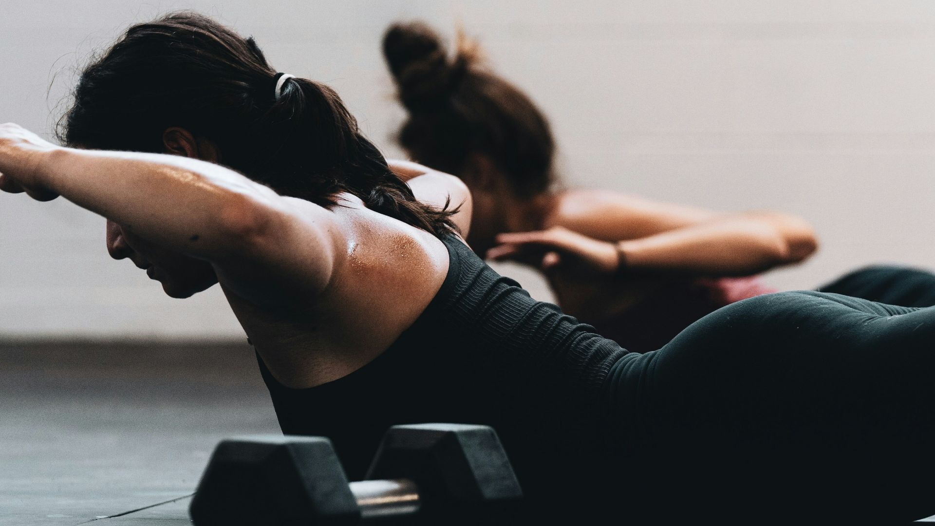 woman in black tank top and black leggings lying on black floor