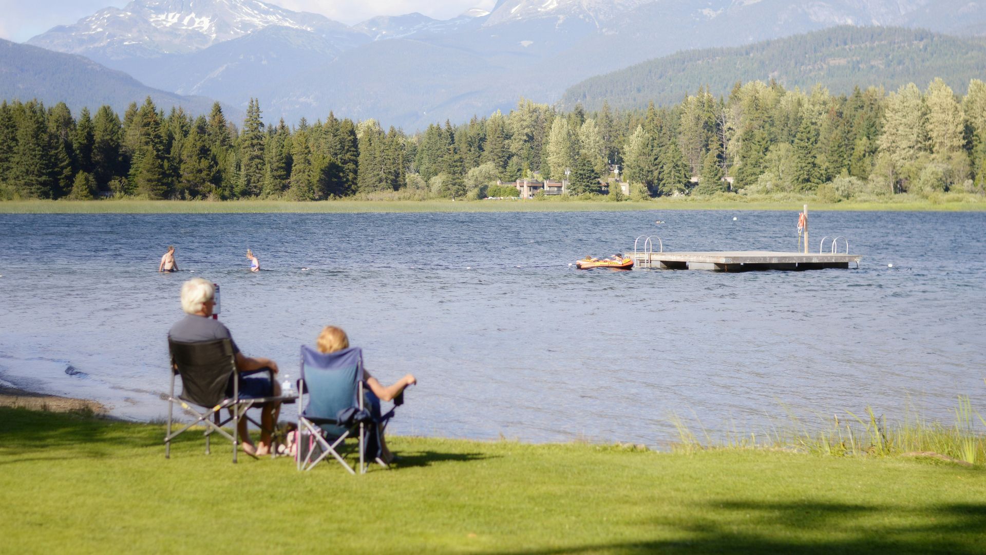 two persons sitting on grass facing the lake