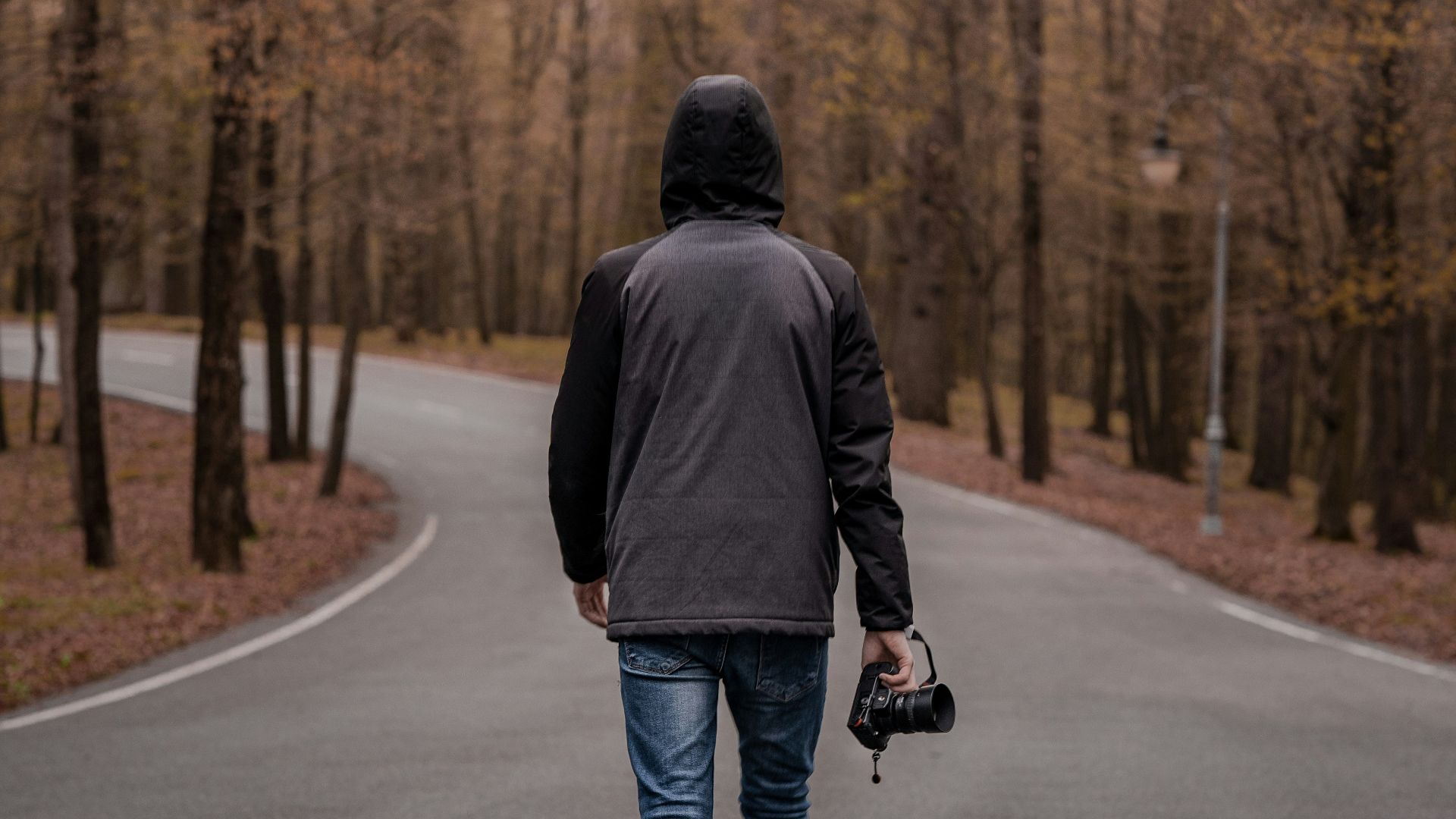 man in black jacket and blue denim jeans walking on road during daytime