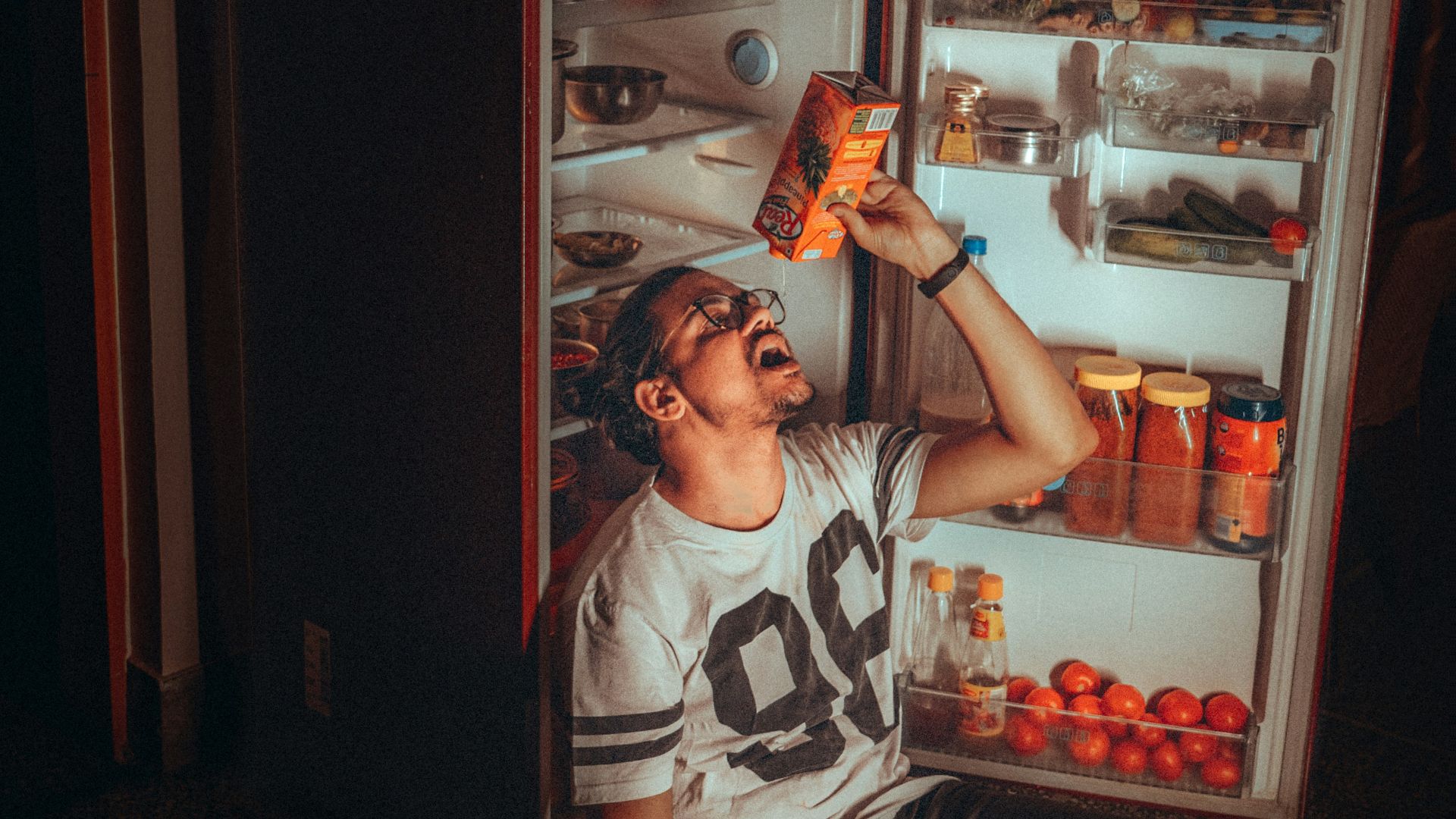 boy in white and black tank top standing beside red top mount refrigerator