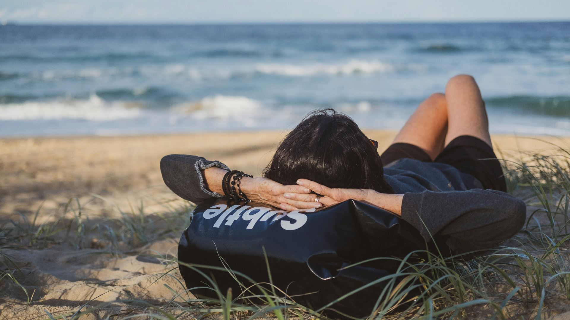 woman lying on grass front of sea at daytime