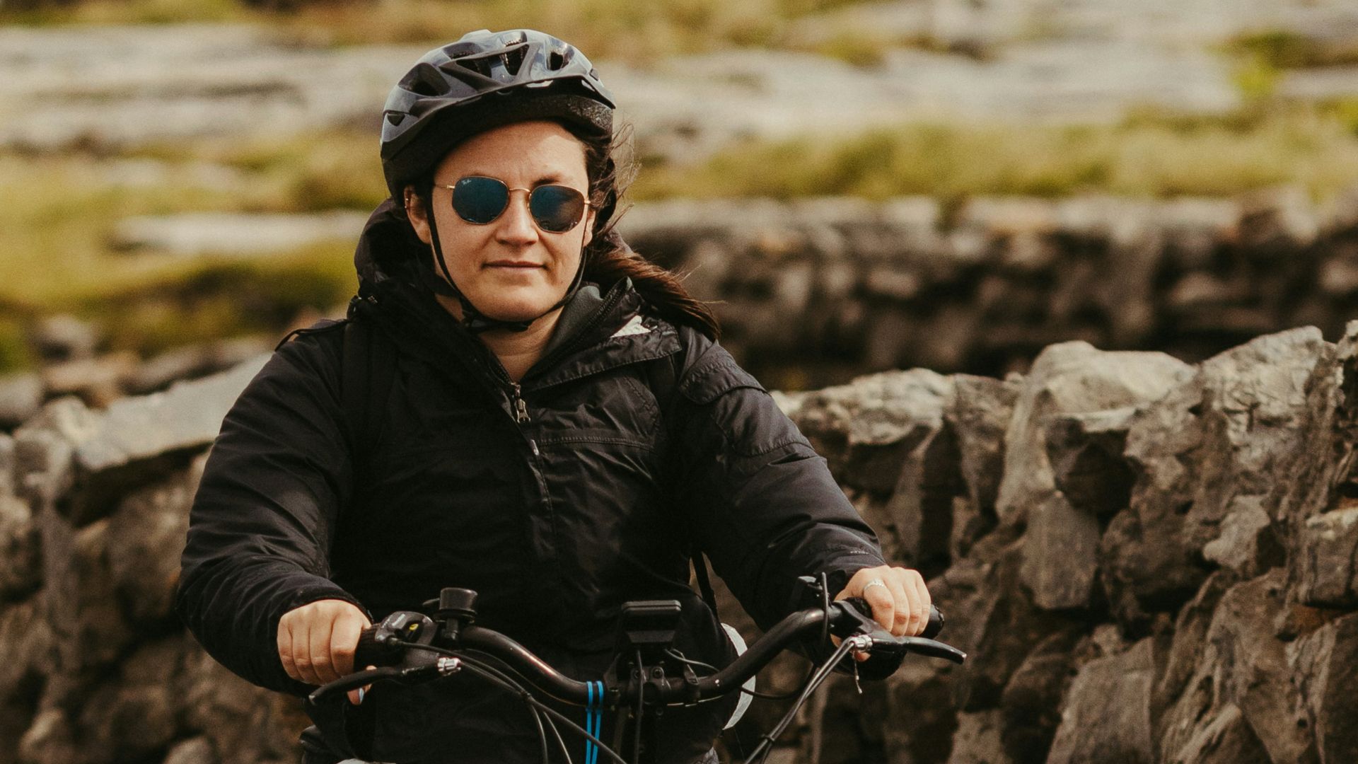 Woman riding bicycle past stone wall