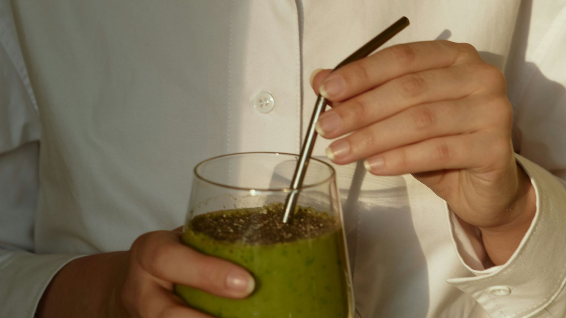 person in white button up shirt holding clear drinking glass with green liquid