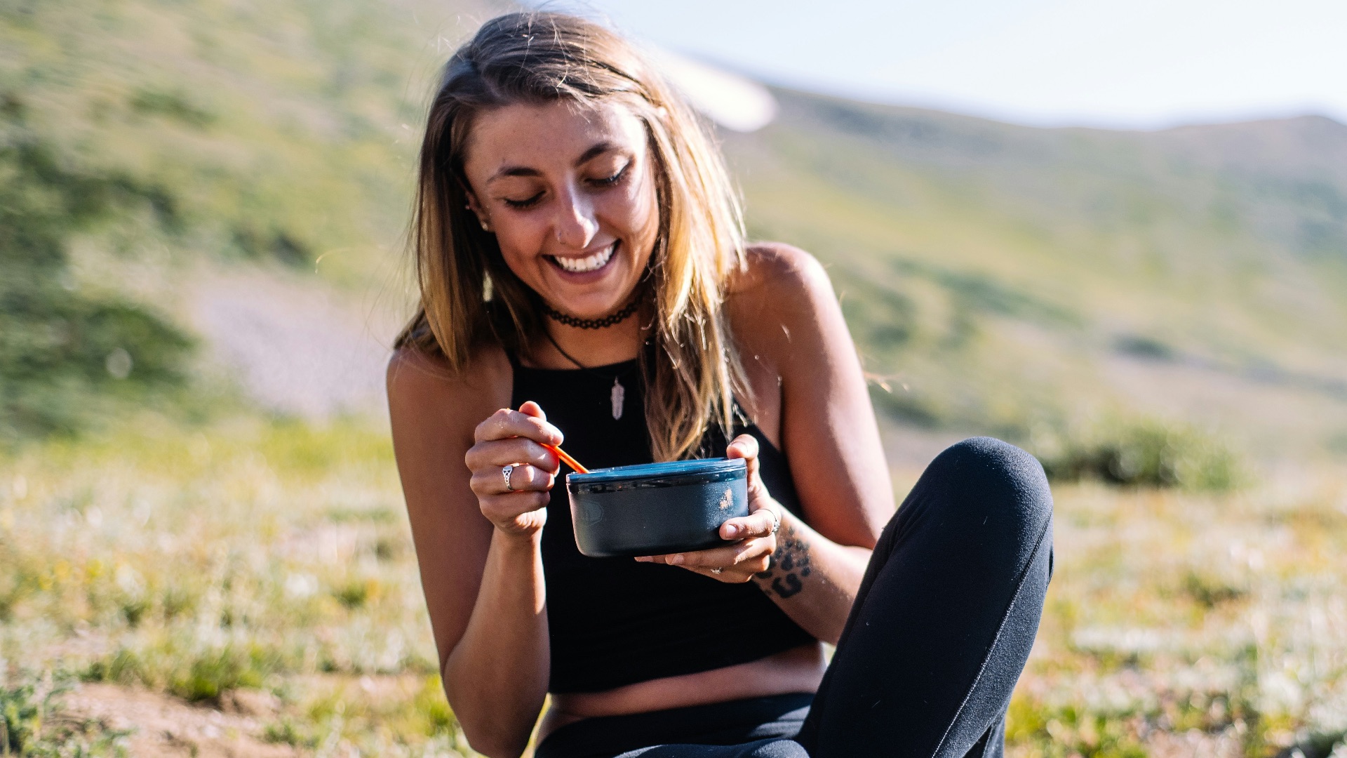 woman in black tank top and black pants sitting on ground holding blue ceramic mug during