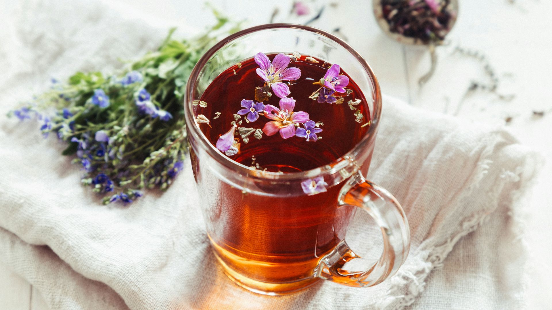 a glass mug filled with tea next to a bunch of flowers