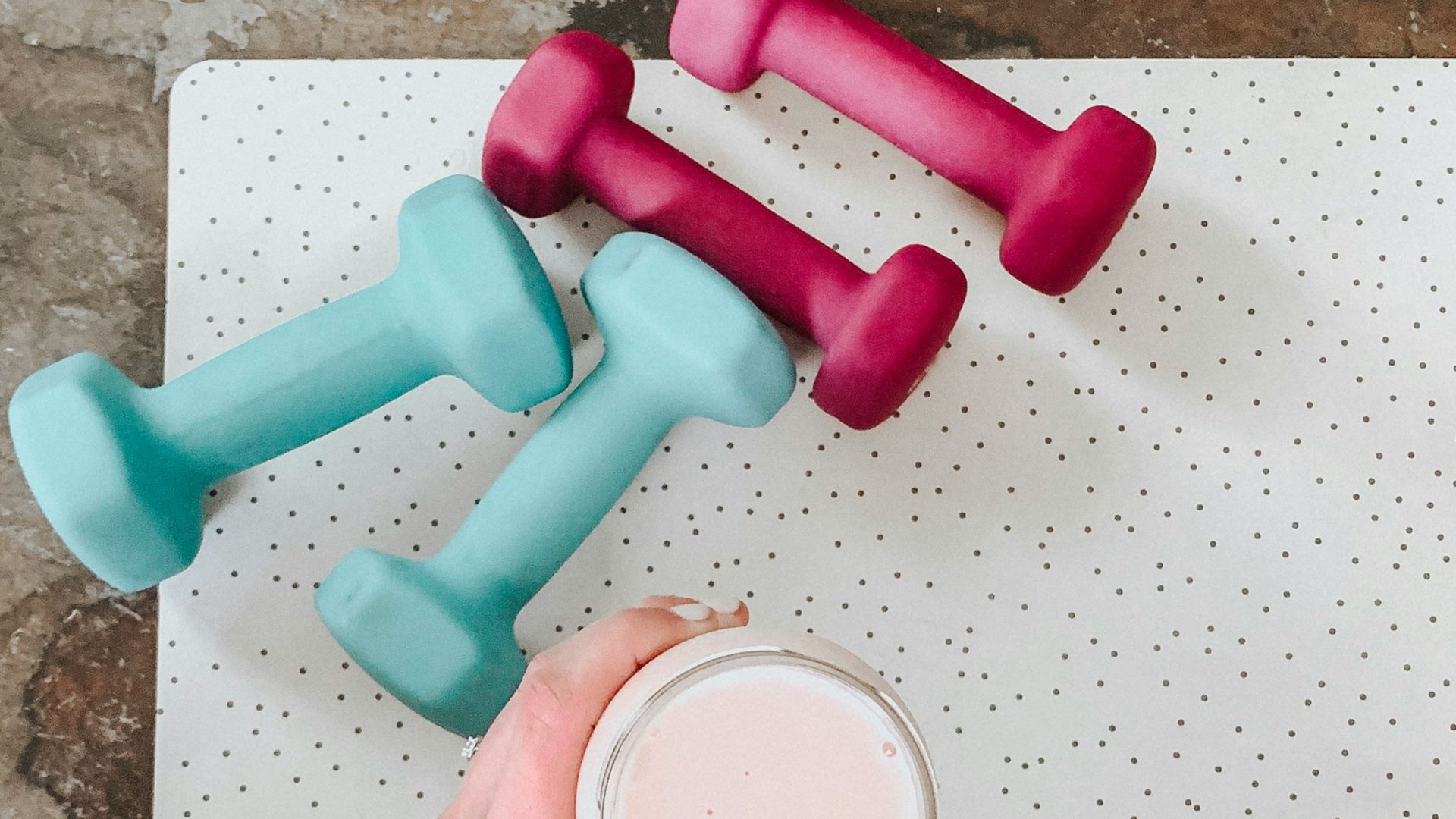 person holding white liquid filled cup above two pairs of dumbbells