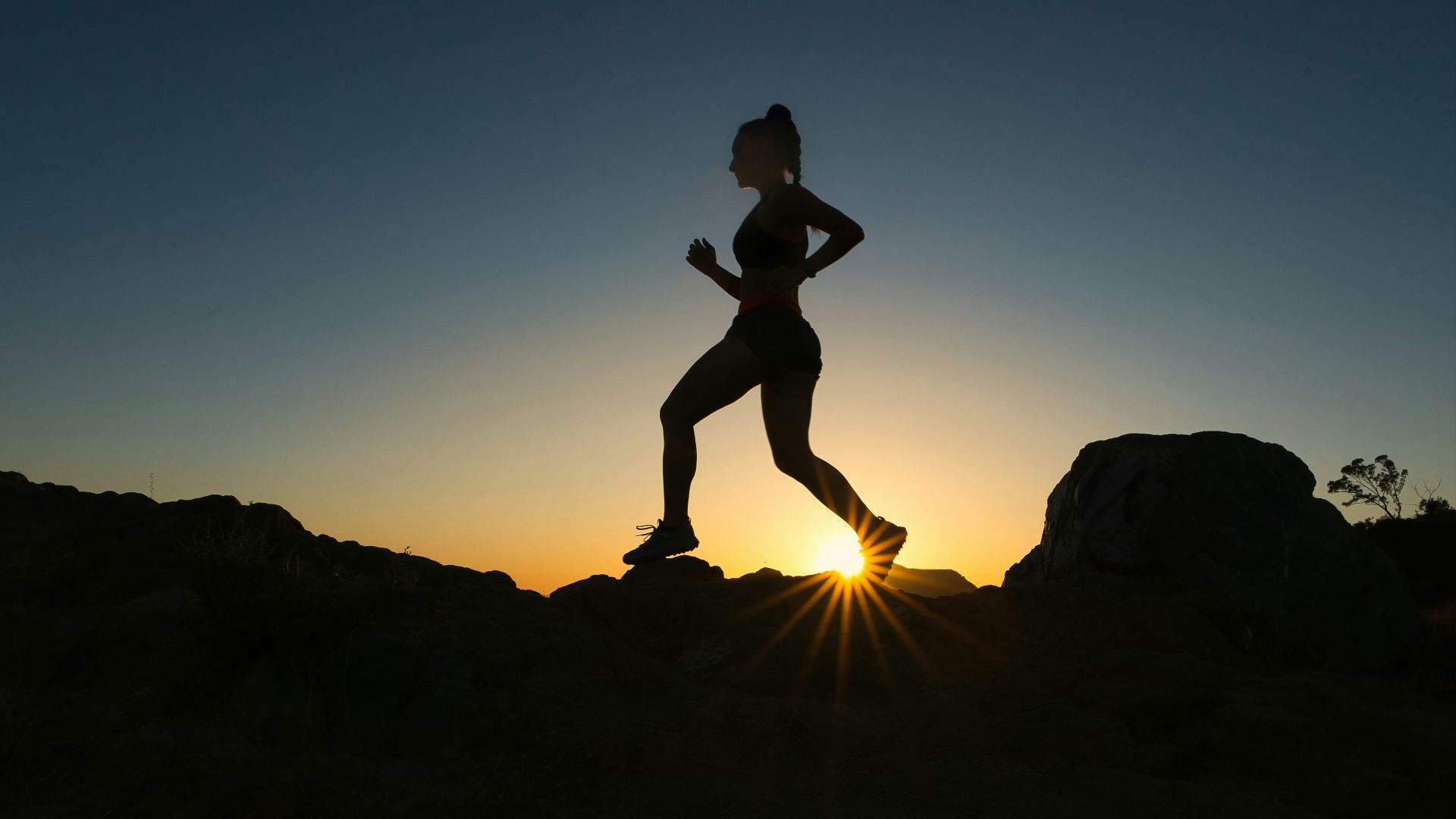 silhouette of man jumping on rocky mountain during sunset