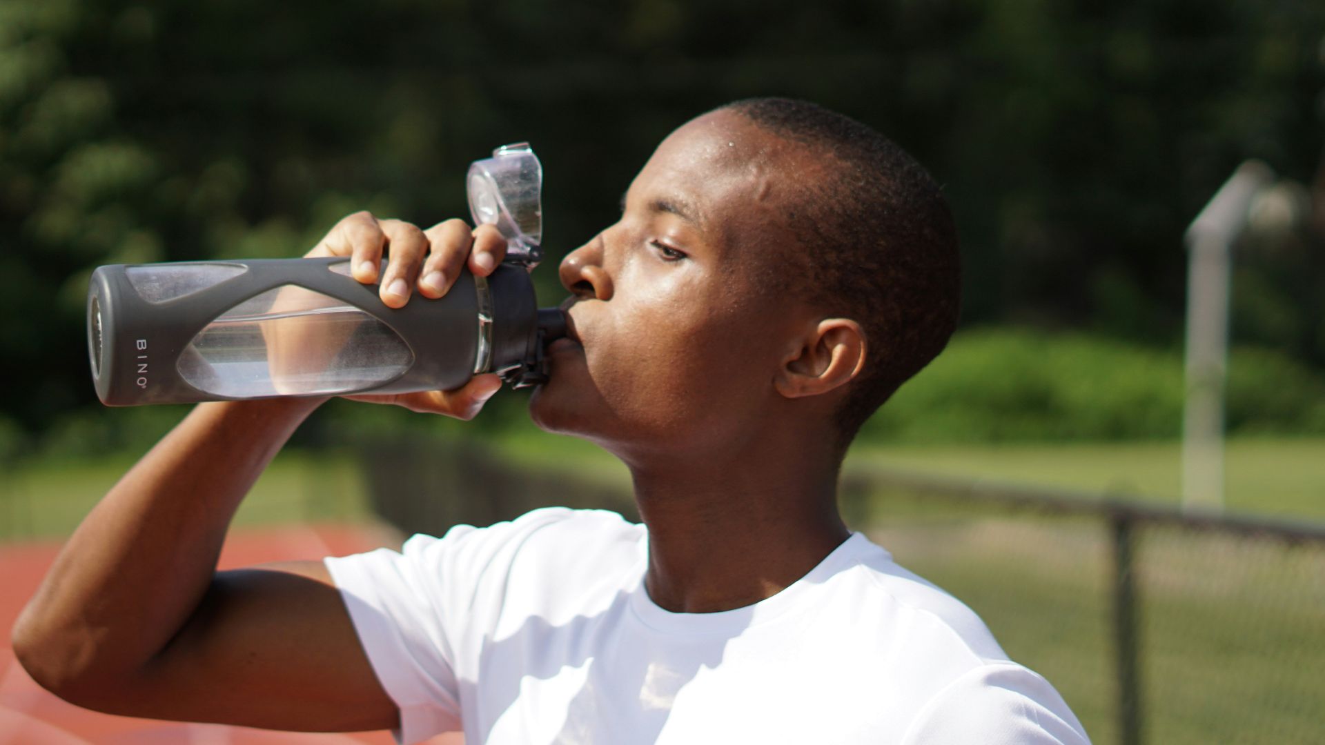 man in white crew neck t-shirt drinking from black sports bottle