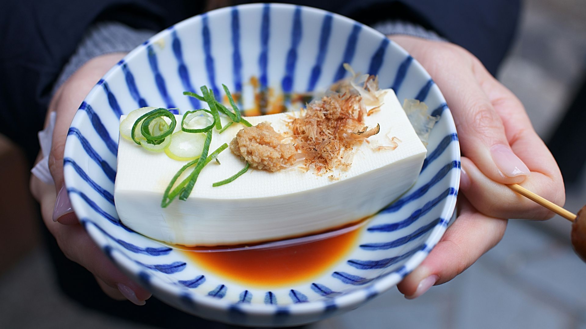 person holding white and blue ceramic plate with rice and sliced cucumber