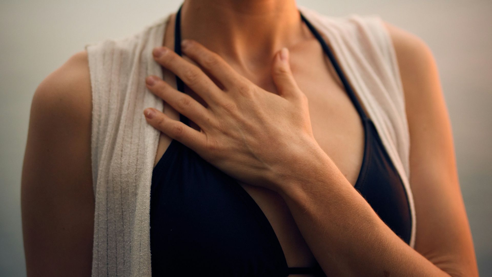 woman in white vest and black bikini with hand on chest