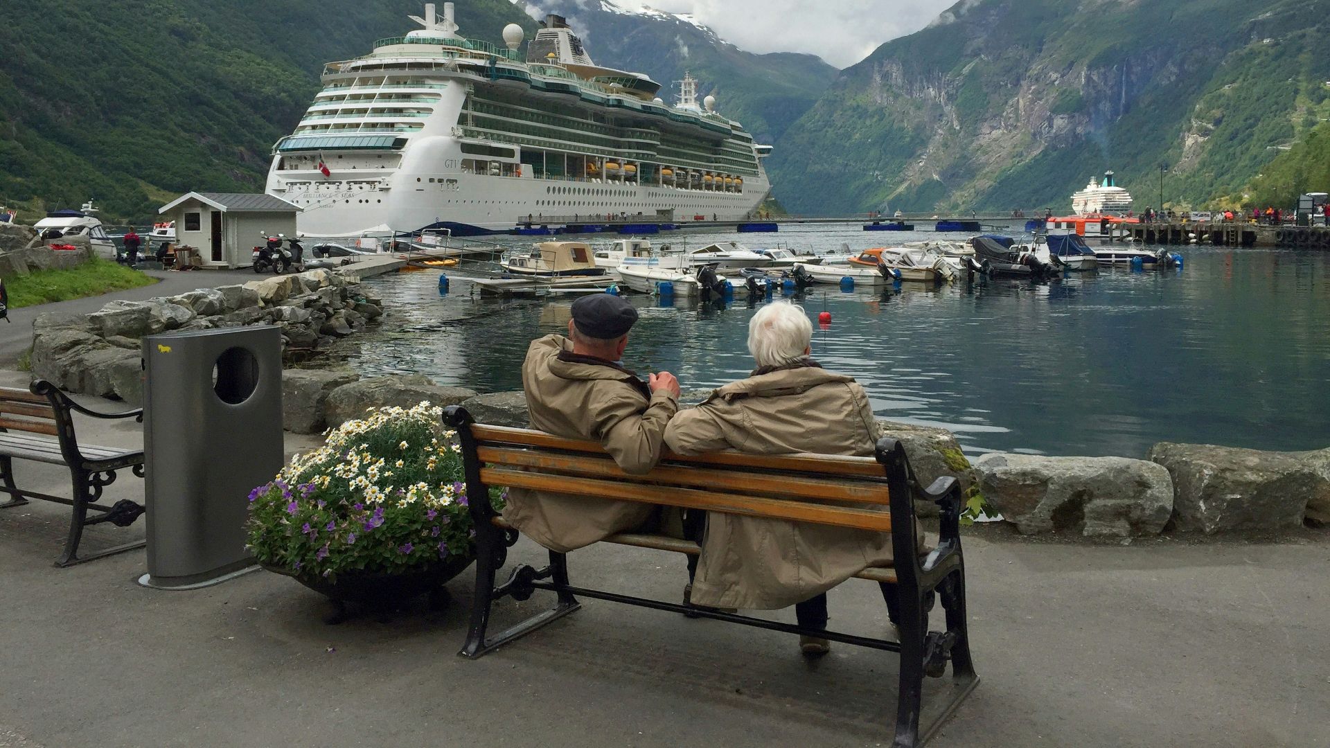 woman in brown coat sitting on brown wooden bench near white cruise ship during daytime