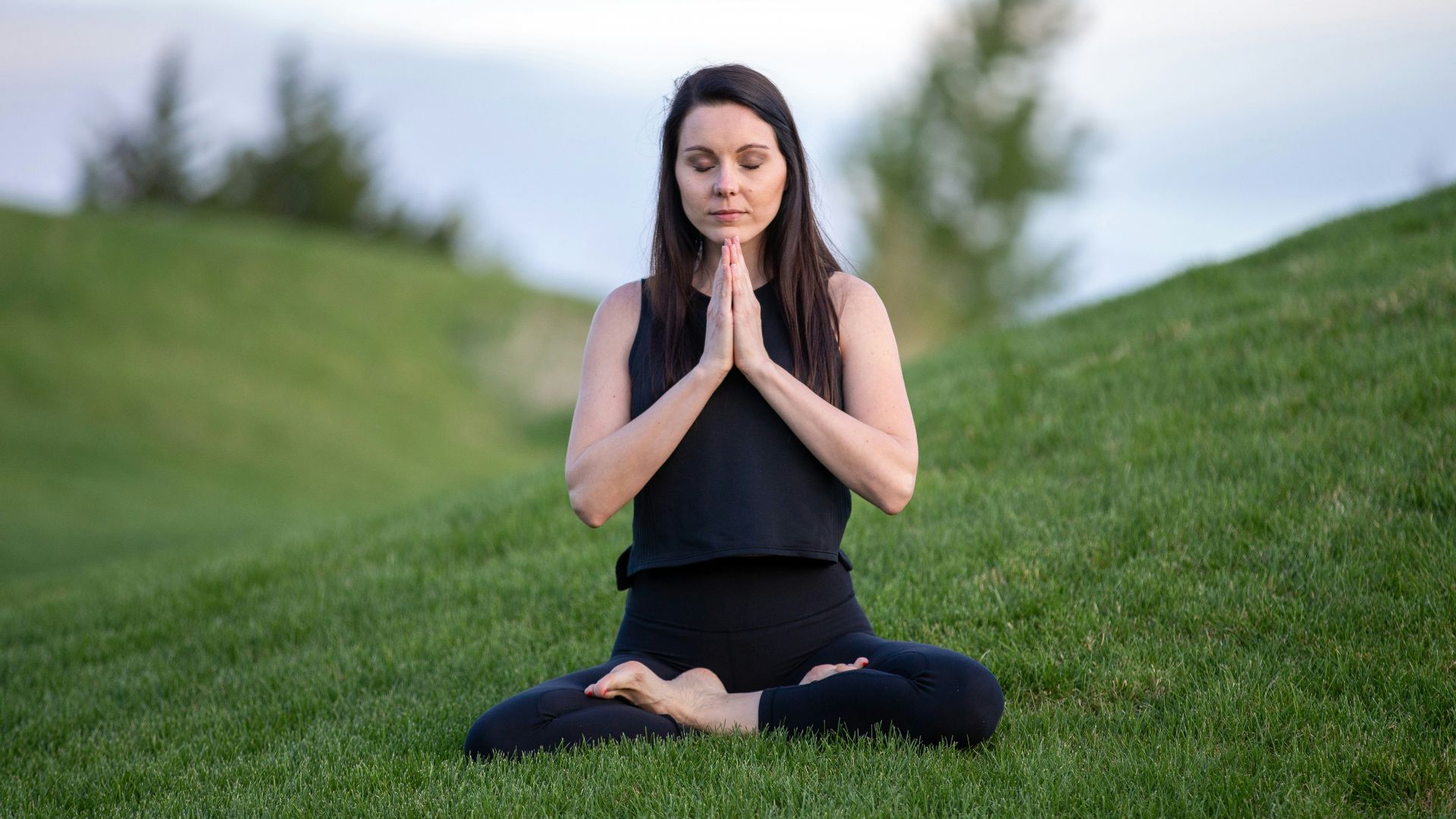 woman in black tank top and black pants sitting on green grass field during daytime
