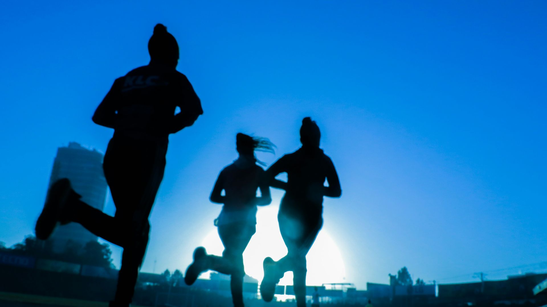 silhouette of three women running on grey concrete road