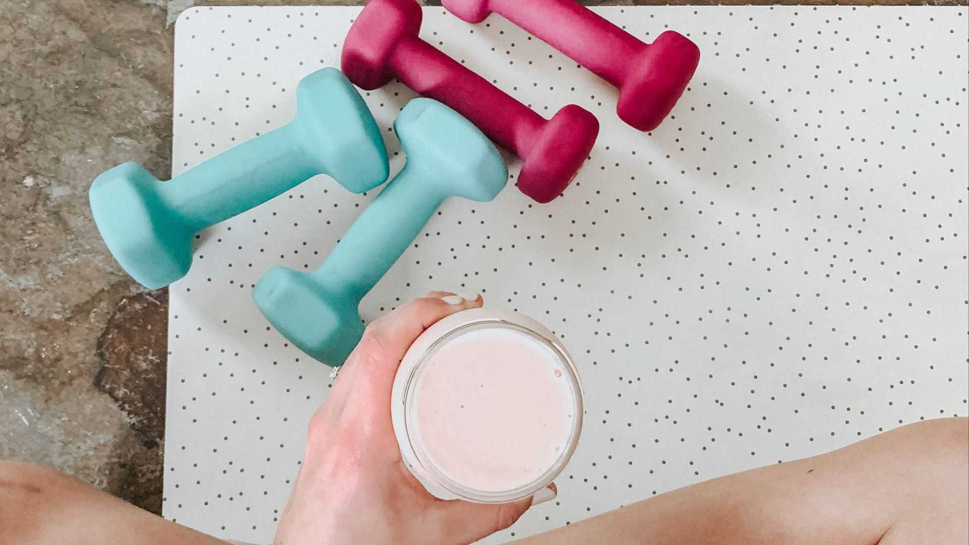 person holding white liquid filled cup above two pairs of dumbbells