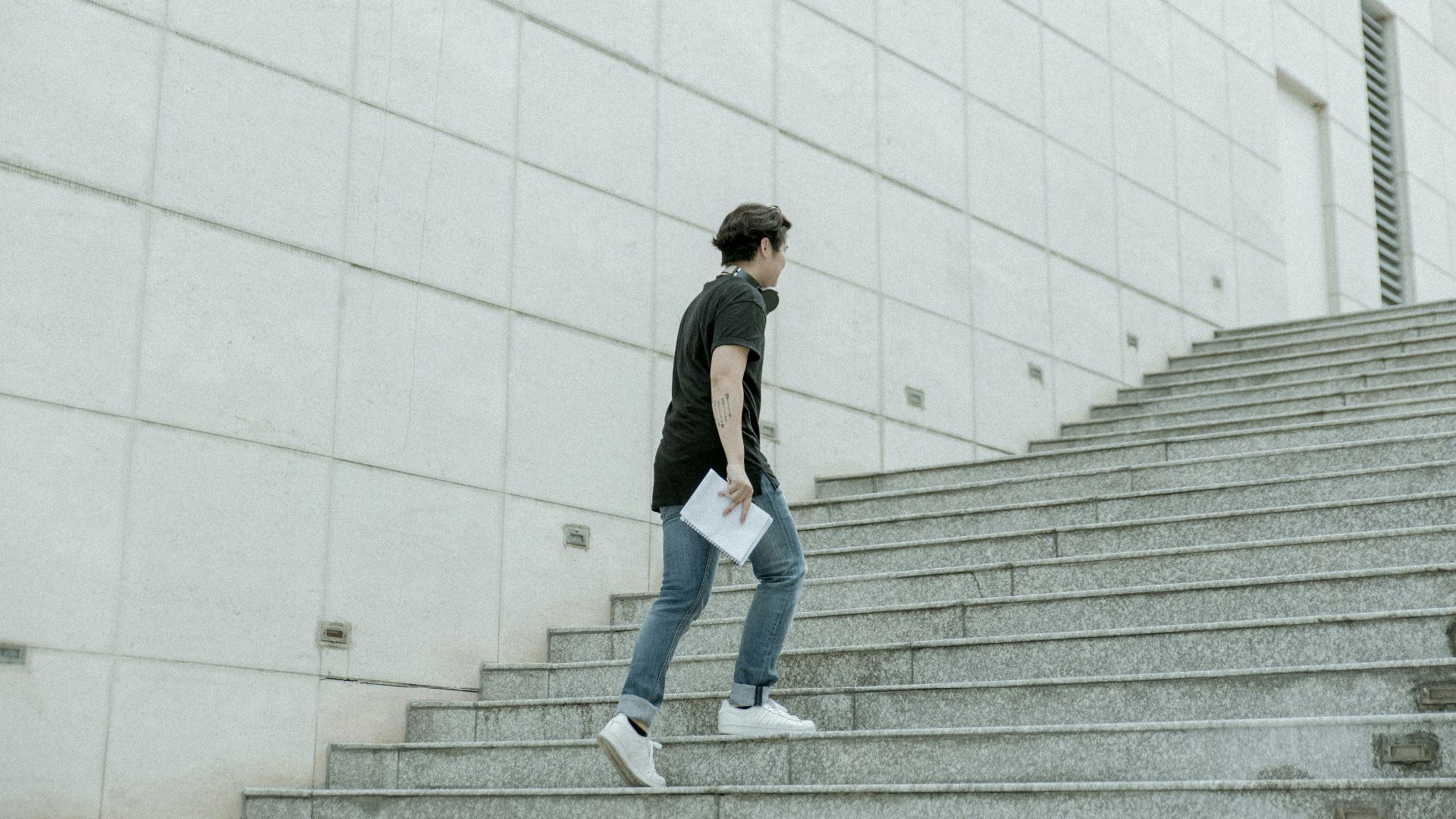 man holding white blanket paper walking on gray stair