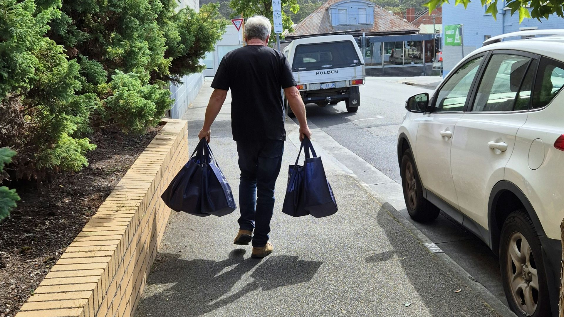 A man walking down a sidewalk carrying two bags