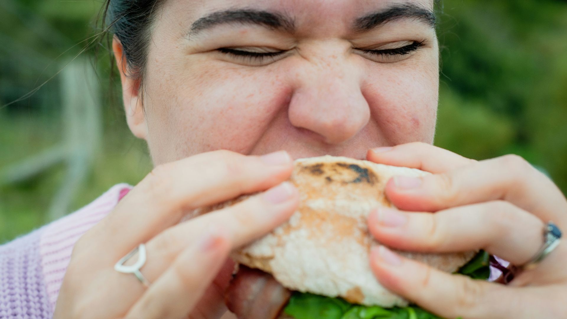 a woman biting into a sandwich with lots of lettuce