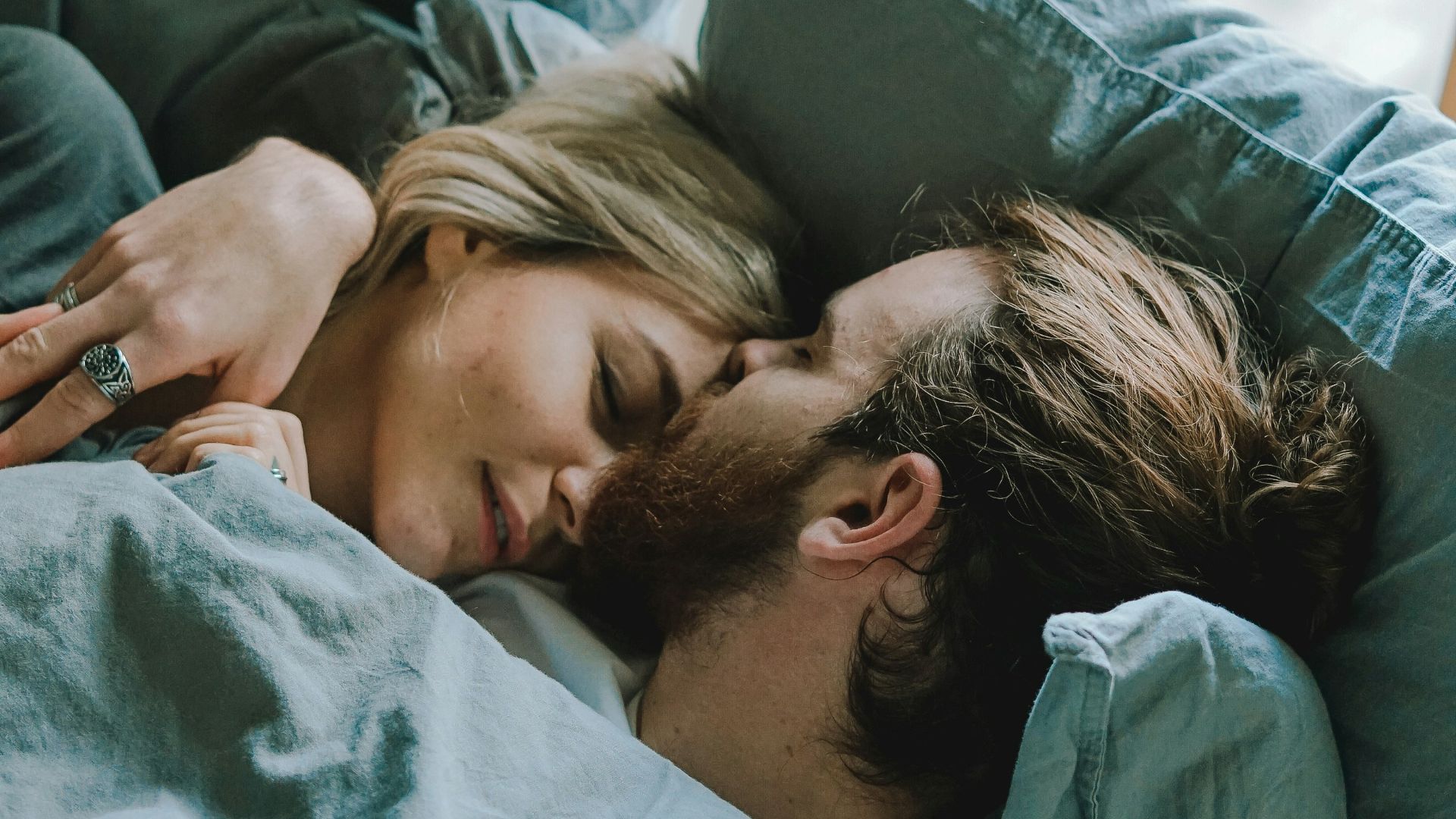 man kissing woman's forehead while lying on bed