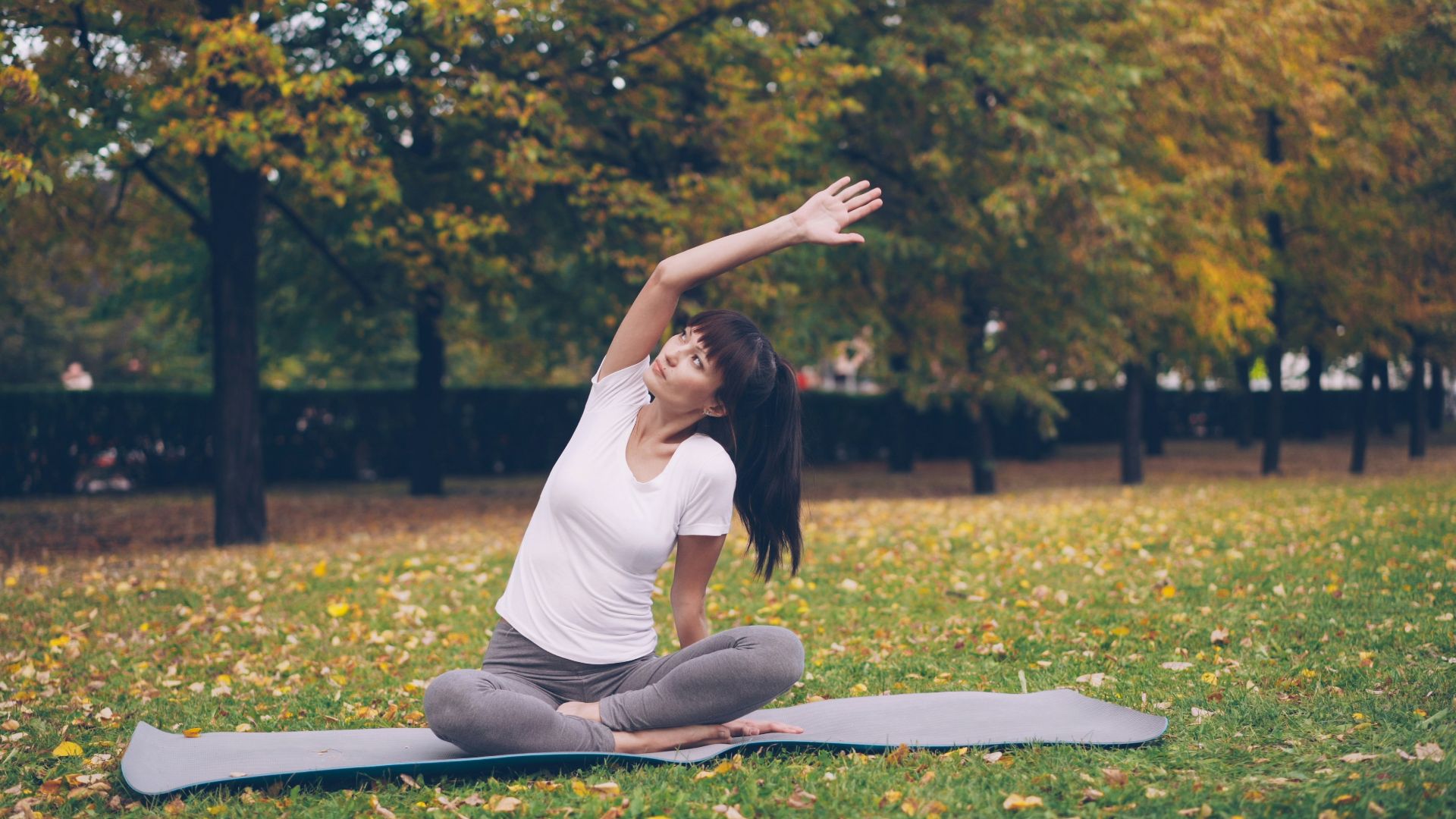 Woman stretching on yoga mat in autumn park
