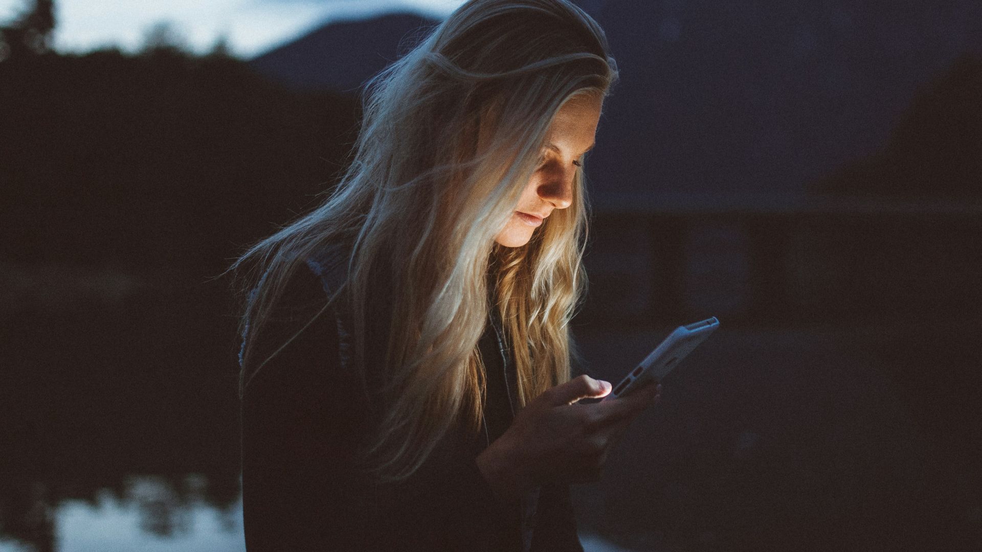 woman looking at phone beside body of water