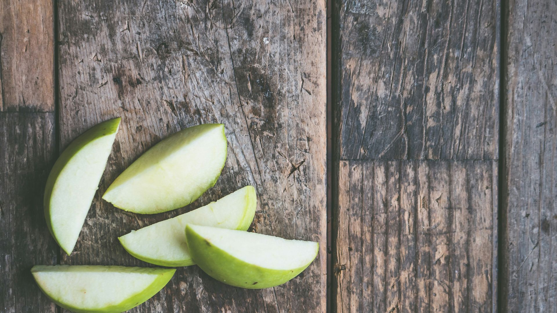 five green apple slices on brown wooden panel