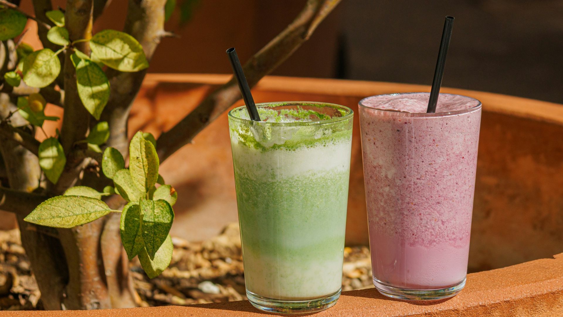 Two colorful smoothies in glasses with straws.