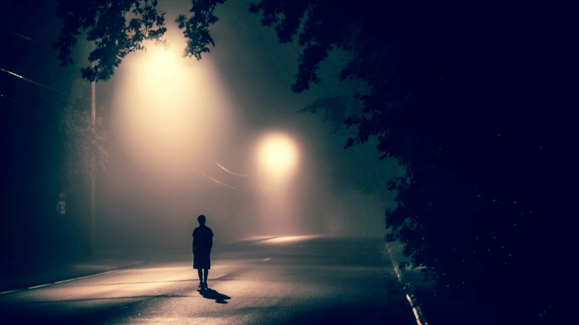 silhouette of person standing on concrete road with streetlights turned on during nighttime