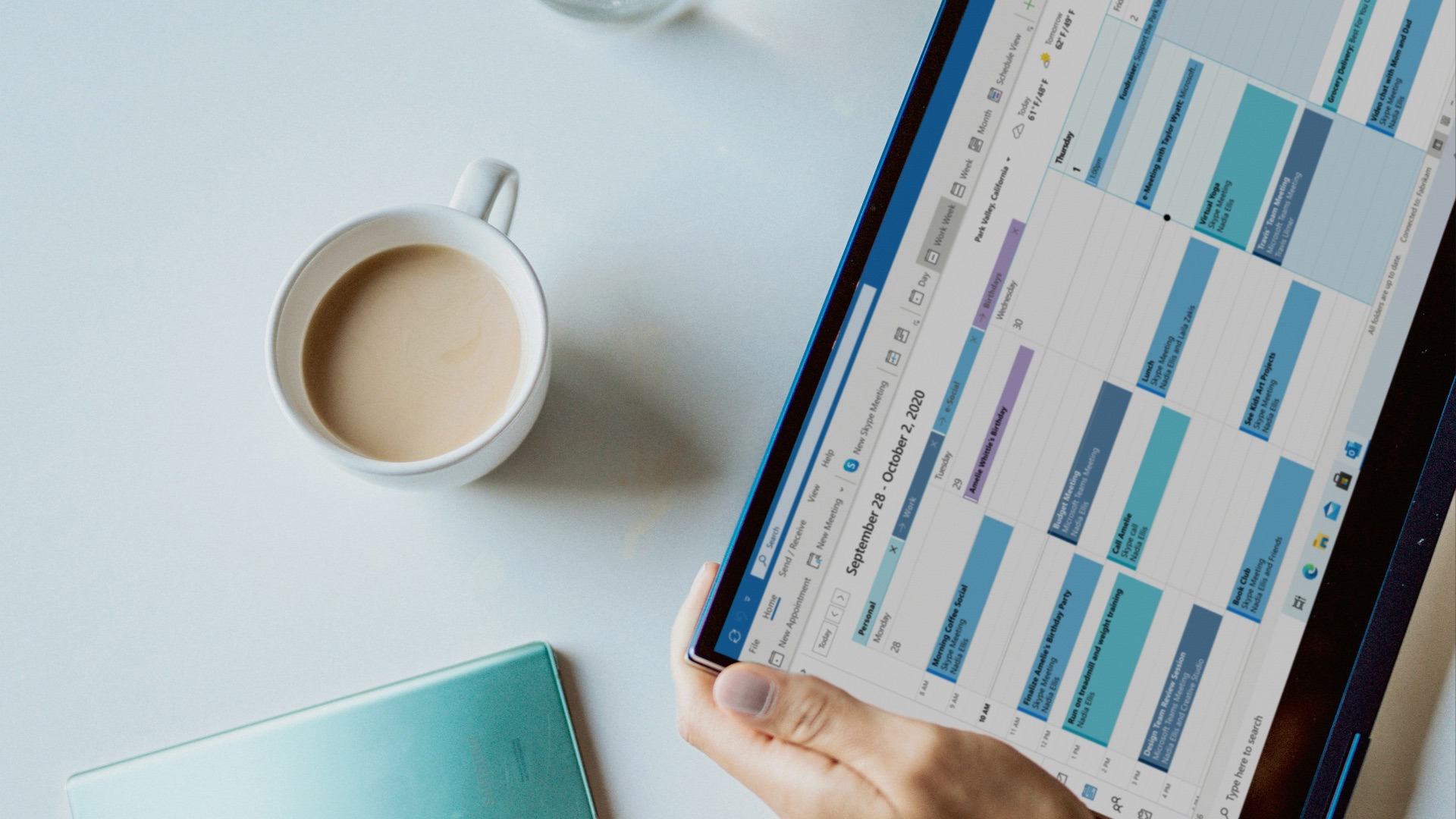 person holding ipad near white ceramic mug and laptop