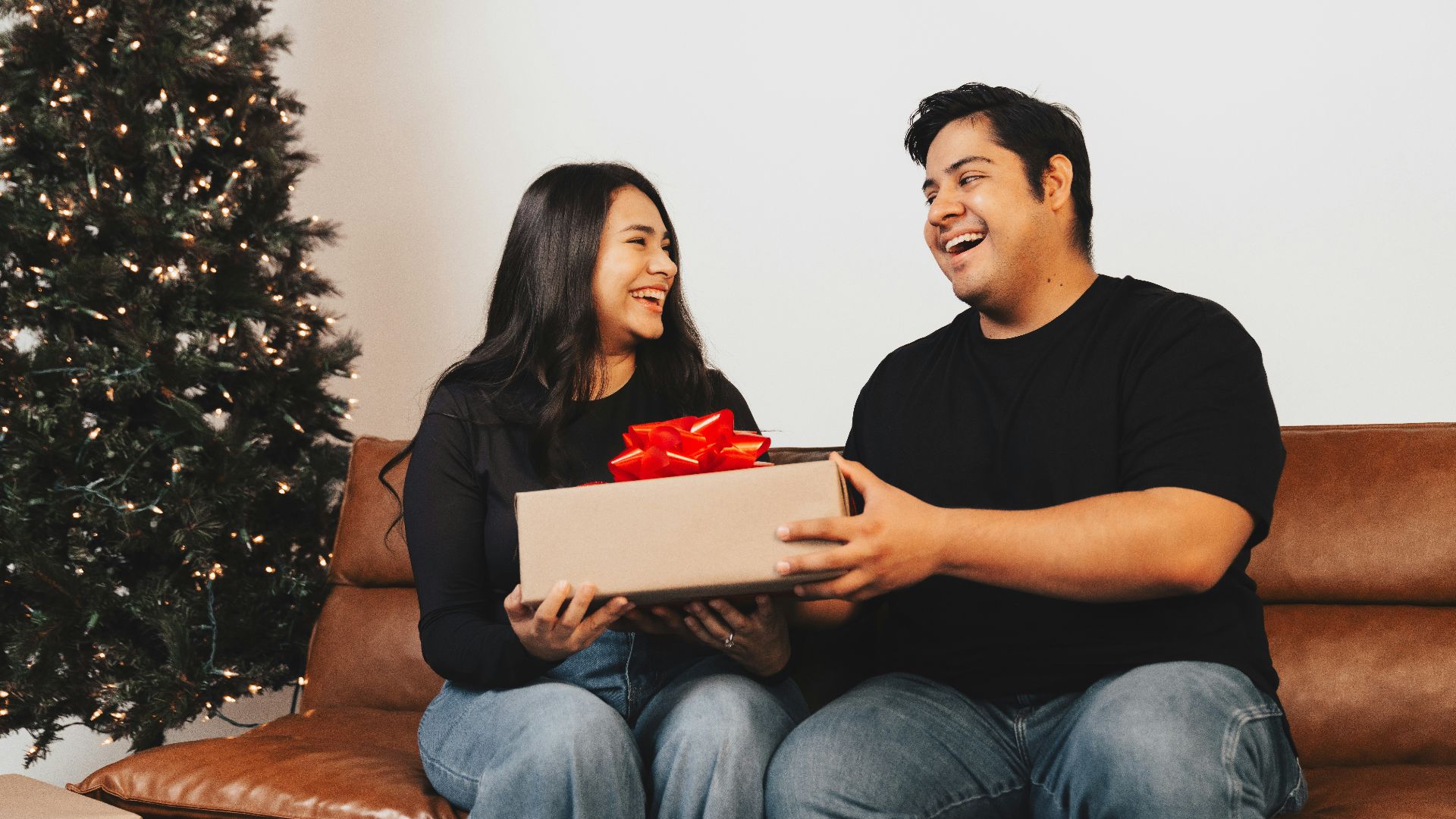 A man and woman sitting on a couch holding a box