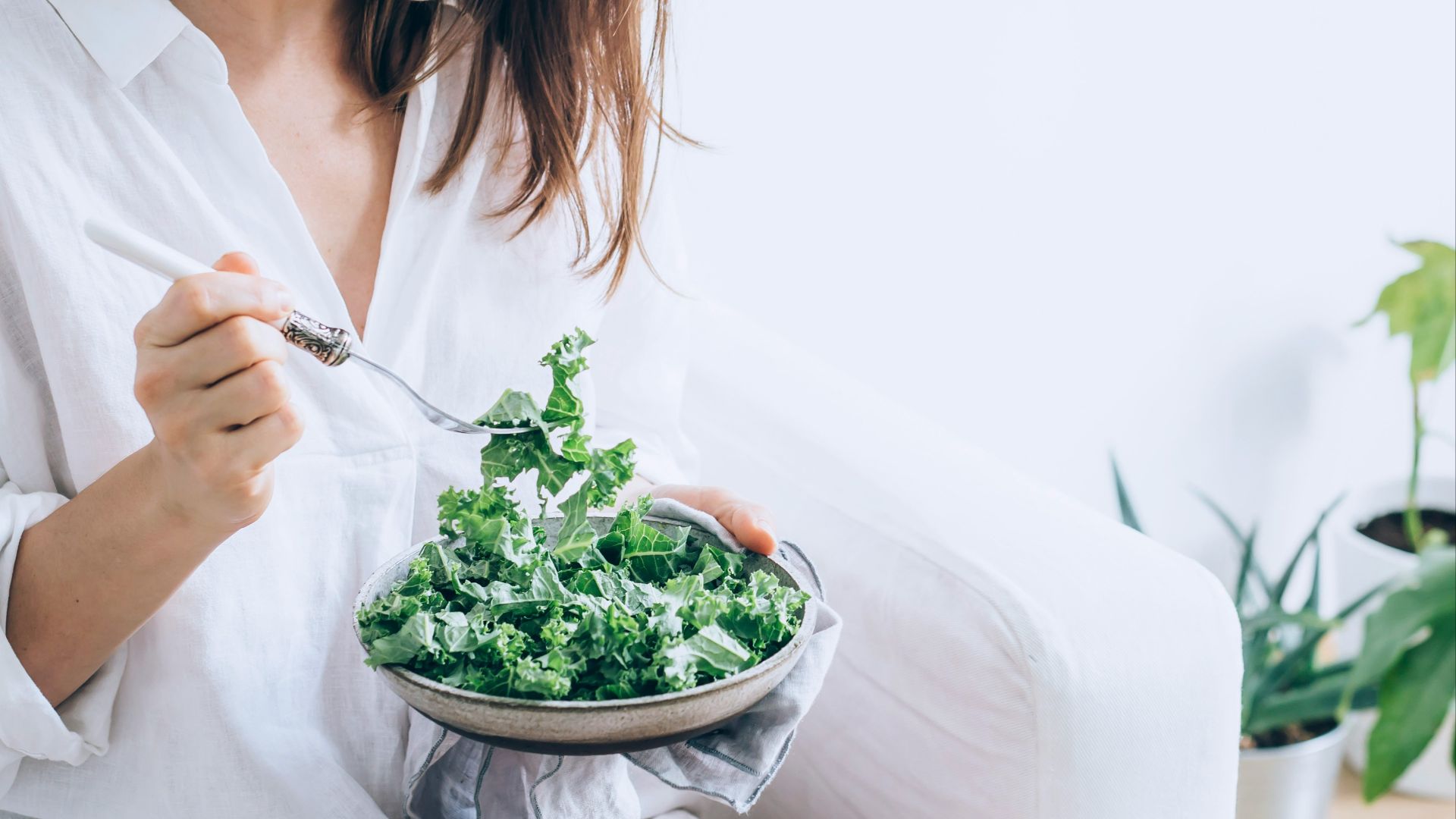 woman in white dress holding silver fork and knife slicing green vegetable on white ceramic bowl