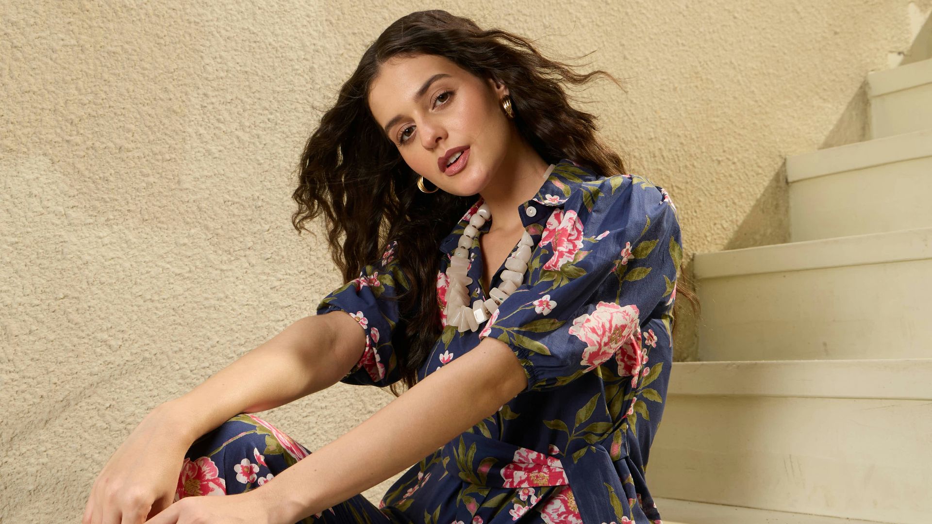 A woman in a floral outfit sits on stairs.