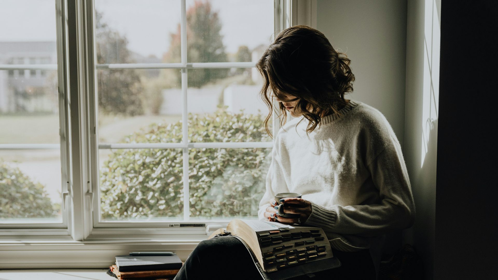 A woman sitting on a window sill reading a book