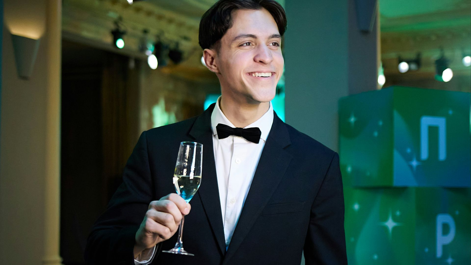 Man in tuxedo holding champagne glass at event.