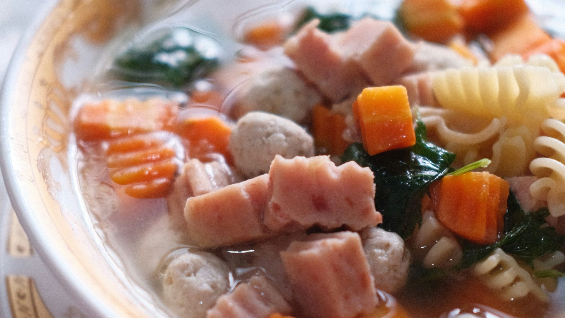 a bowl of soup with pasta, ham, and spinach