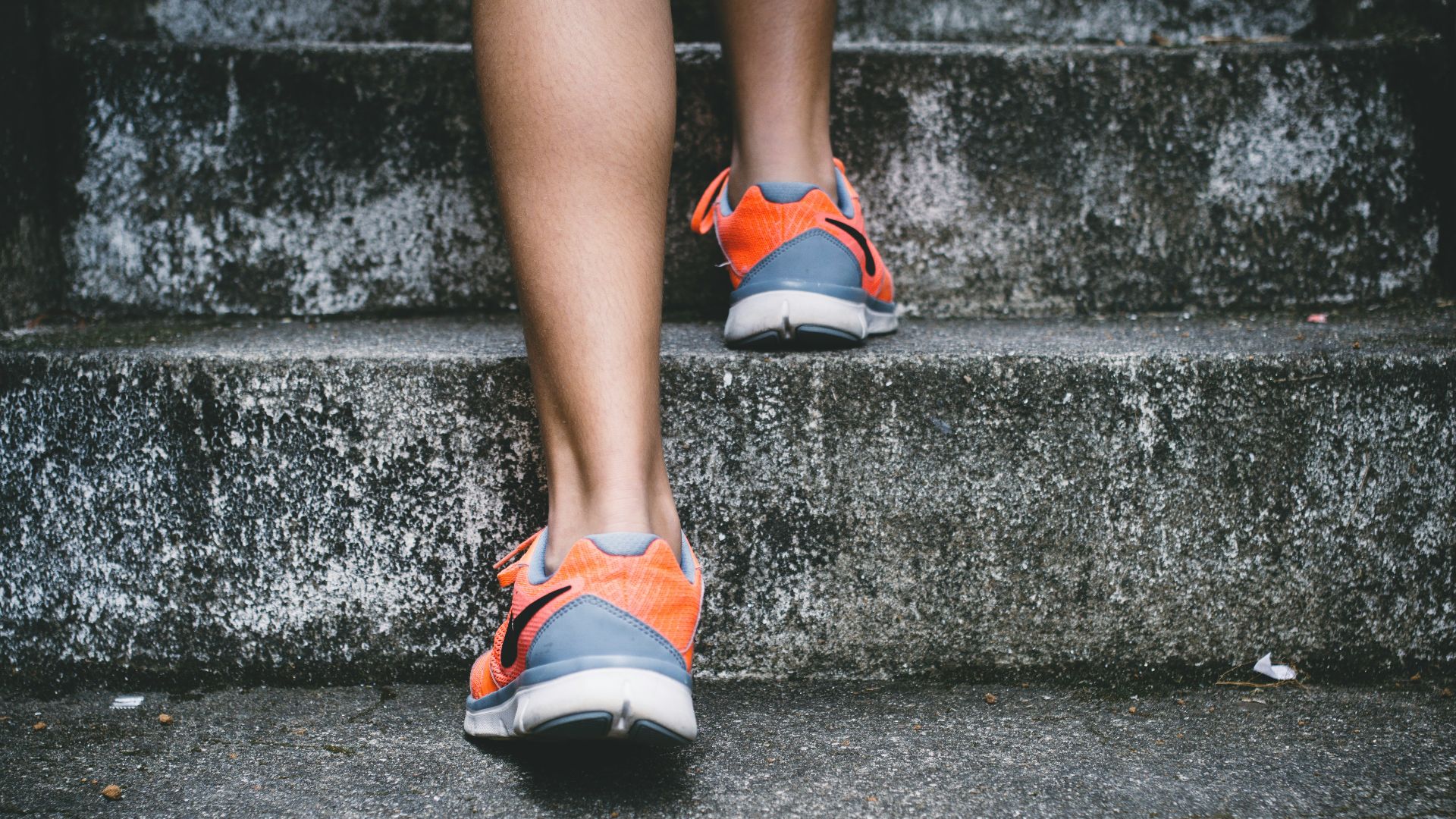 person wearing orange and gray Nike shoes walking on gray concrete stairs
