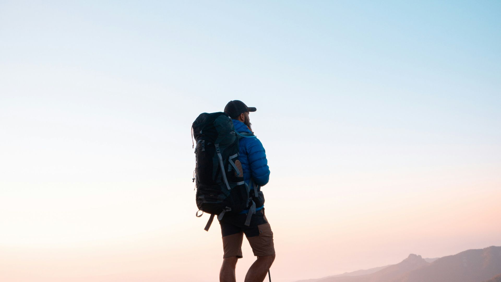 man in black jacket and blue denim shorts with black hiking backpack standing on mountain during