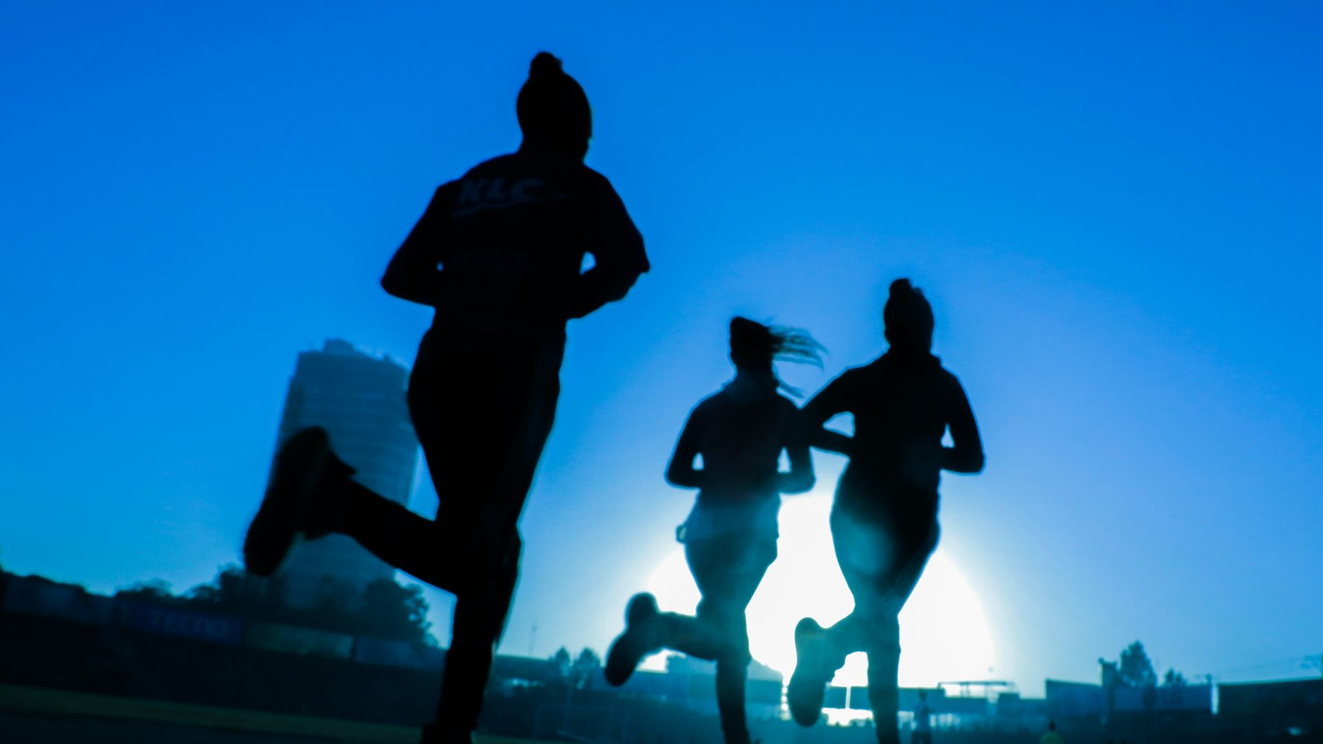 silhouette of three women running on grey concrete road