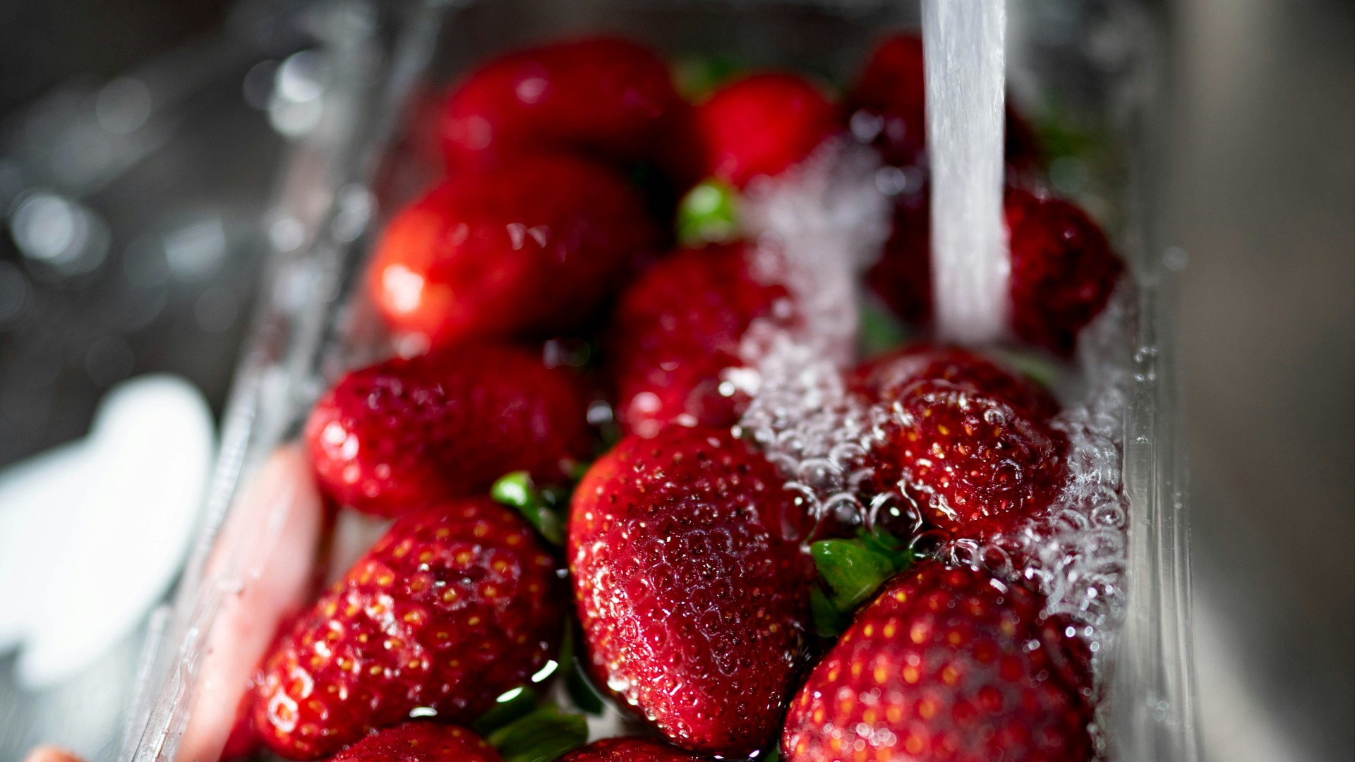 water poured into red strawberries in plastic tray