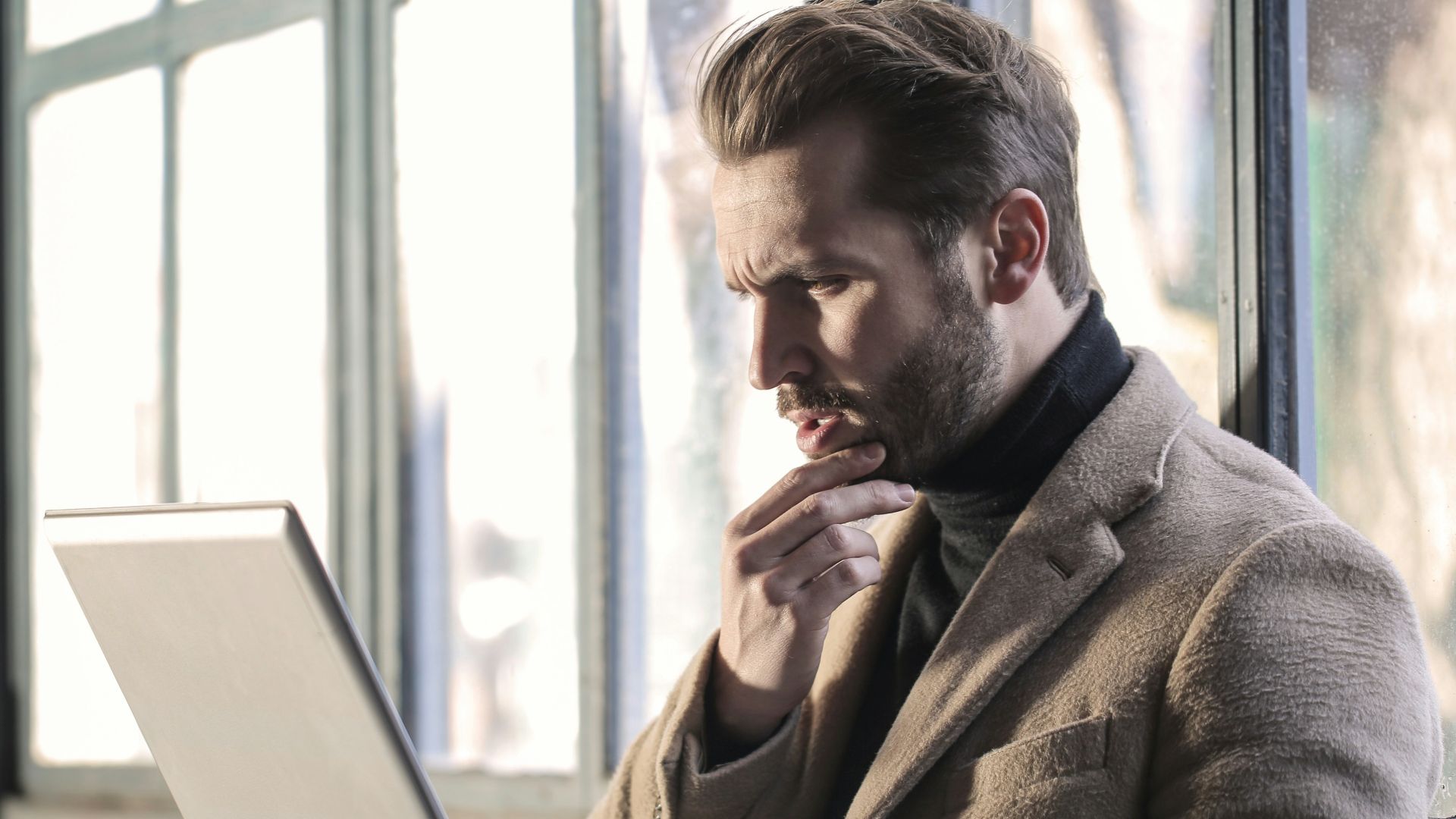 man holding his chin facing laptop computer