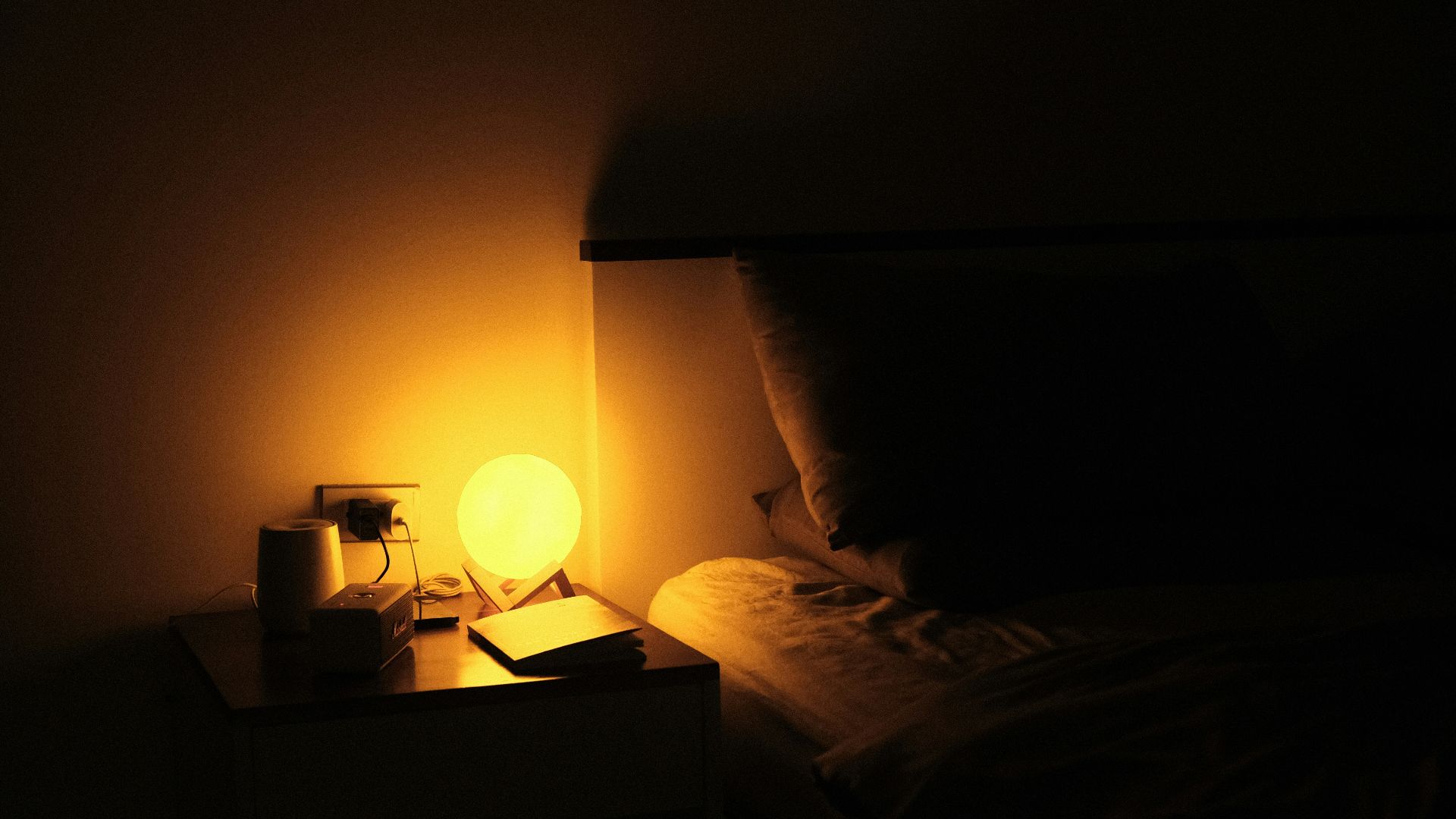 a night stand with a lamp on it next to a bed