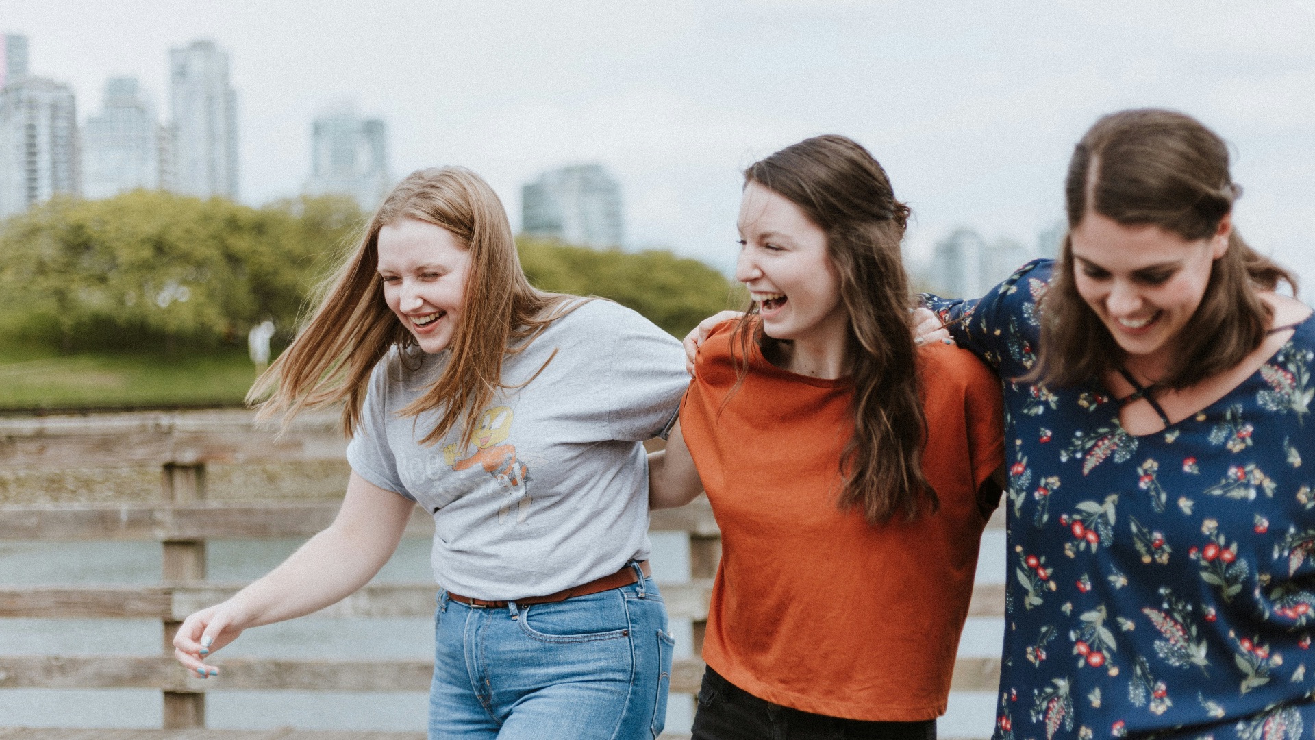 three women walking on brown wooden dock near high rise building during daytime