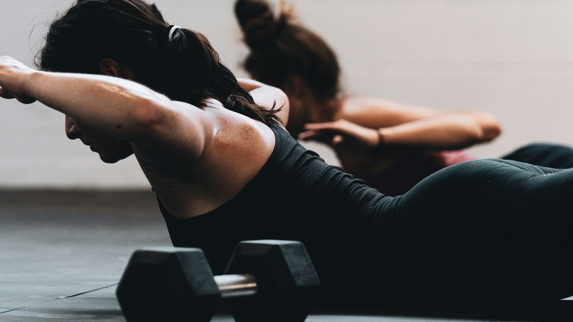 woman in black tank top and black leggings lying on black floor