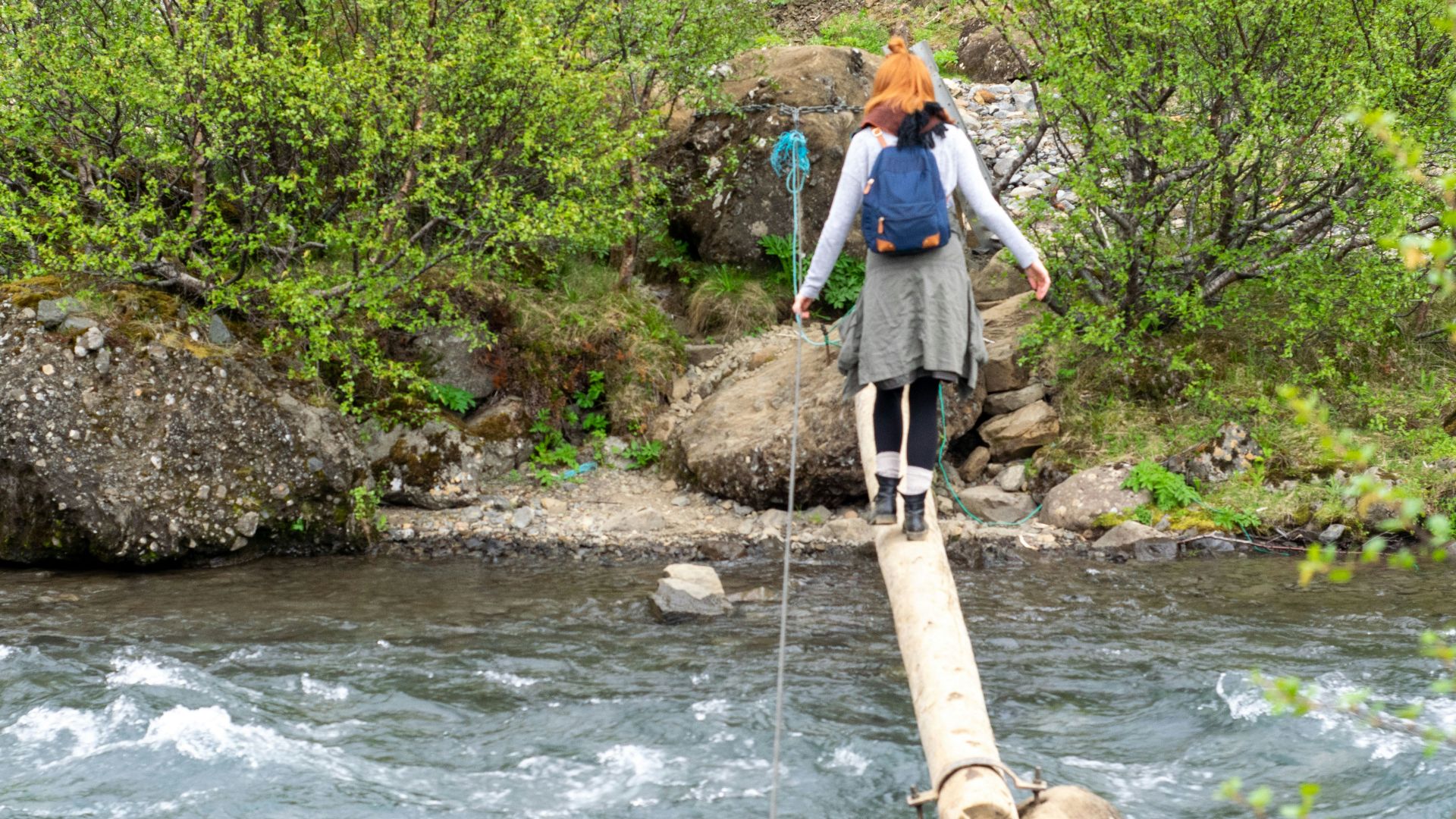a woman walking across a wooden bridge over a river
